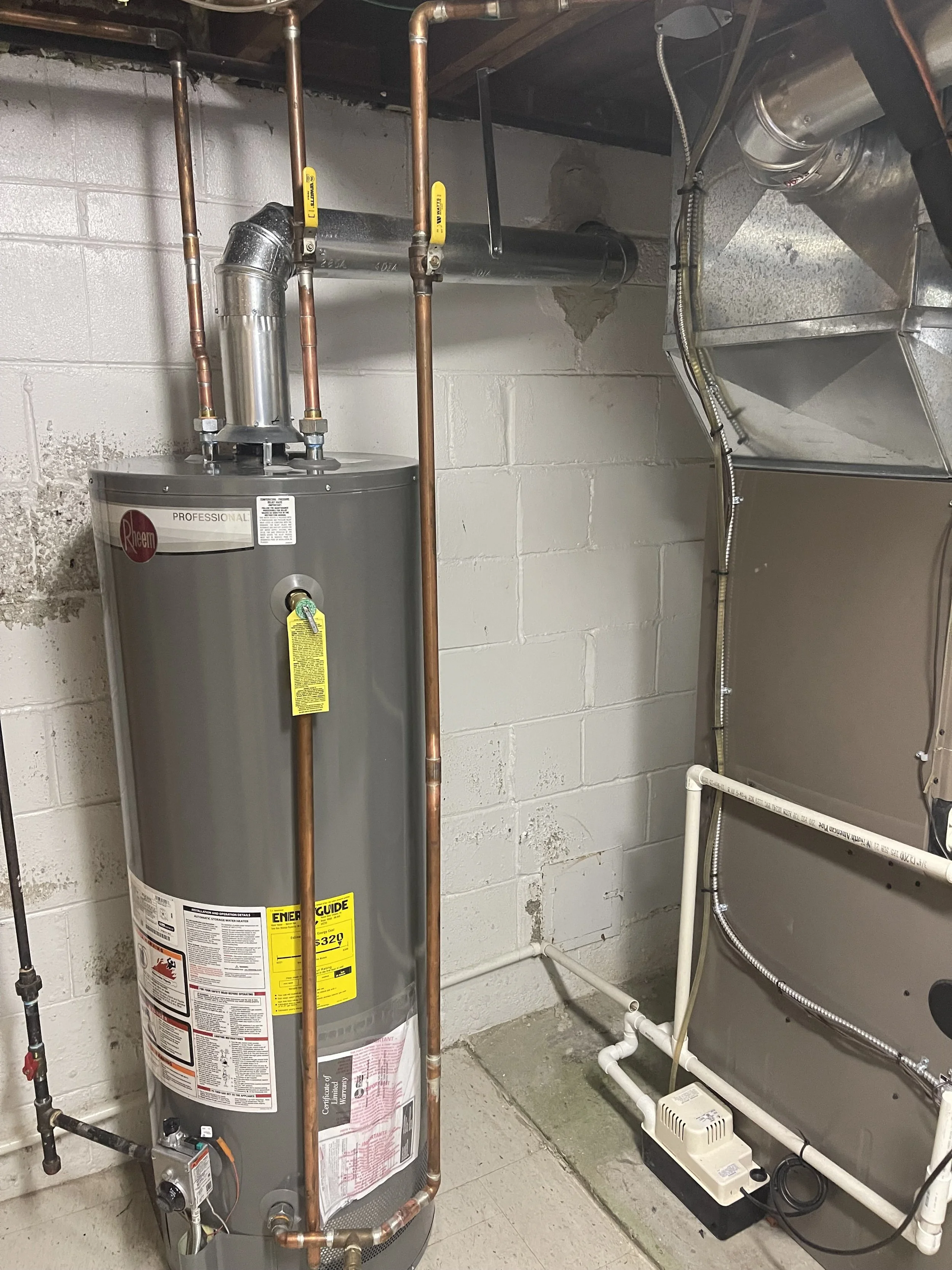A water heater with copper pipes and a vent pipe in a basement utility room.