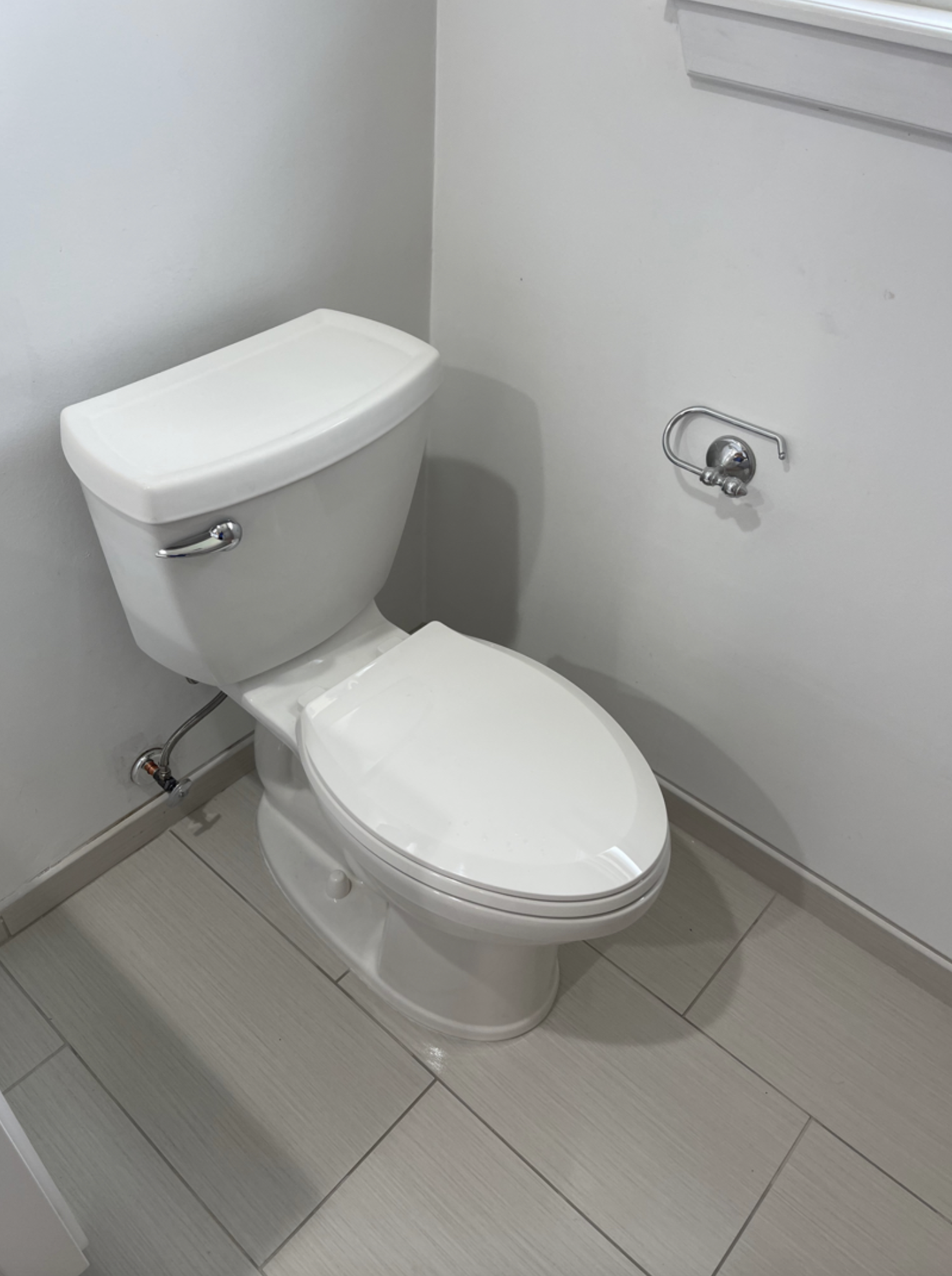 Clean white toilet with closed lid in a small bathroom, with a gray wall and beige tiled floor.