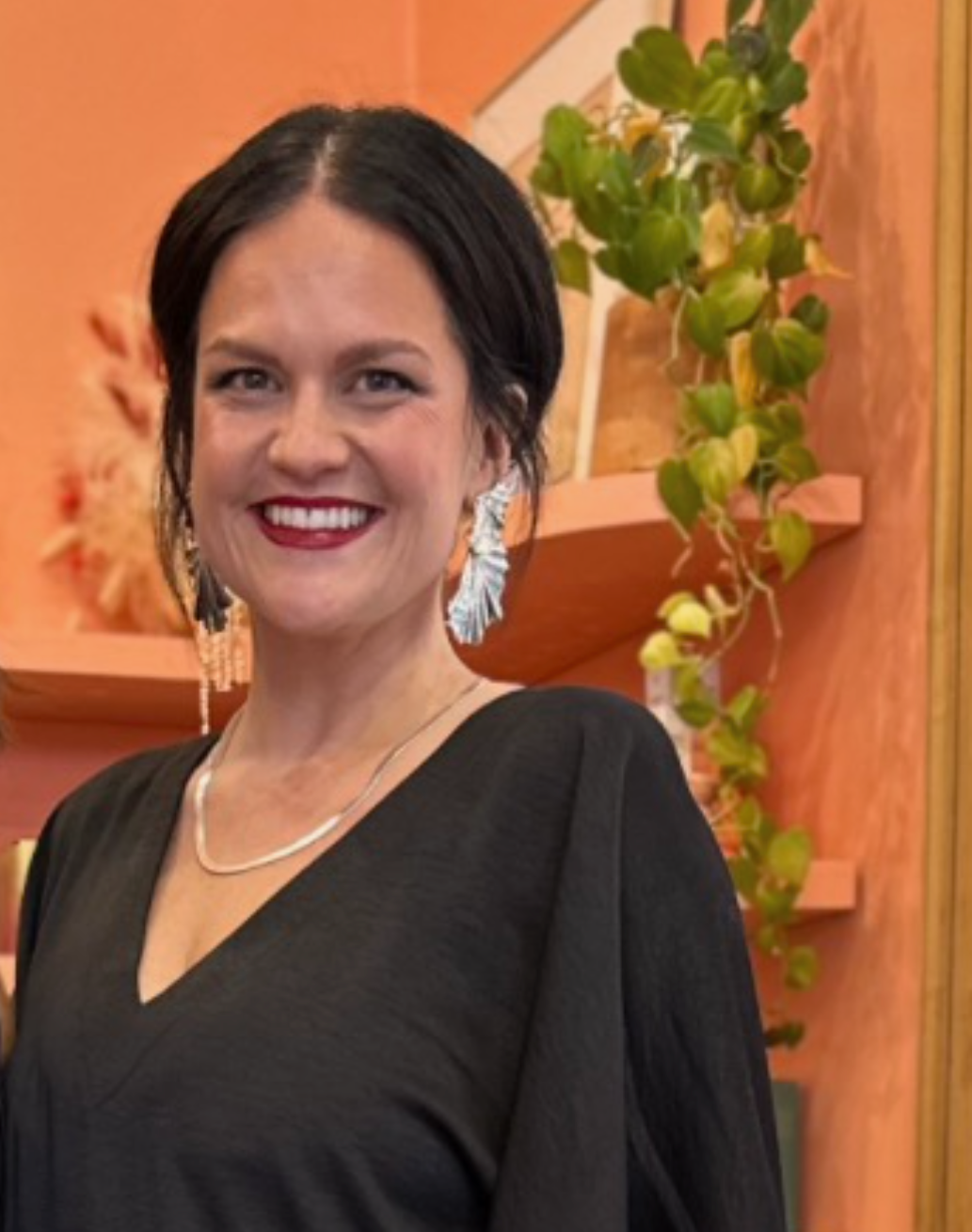 Woman smiling at camera wearing a black shirt and long earrings