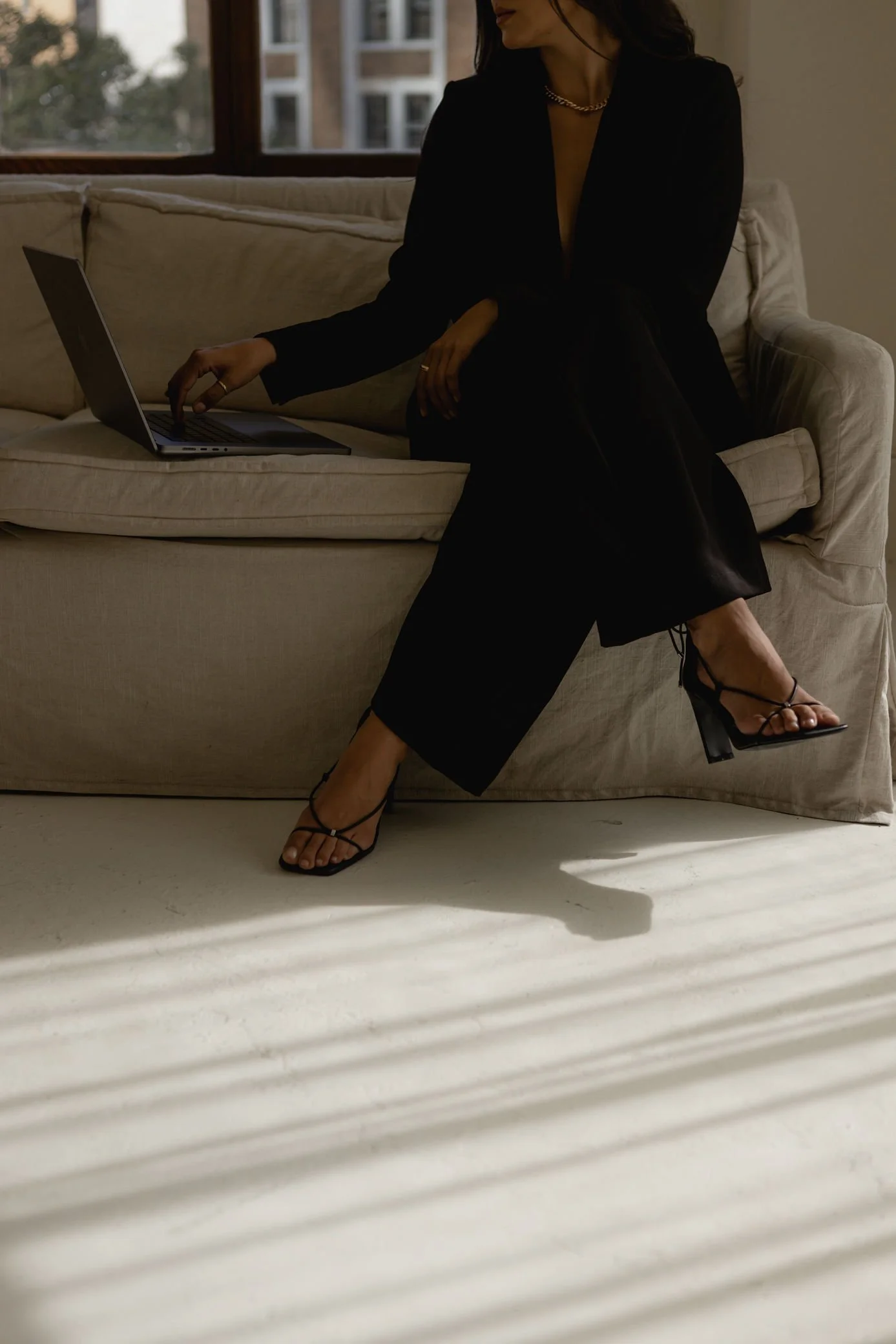 Woman in black suit sitting on couch next to her laptop