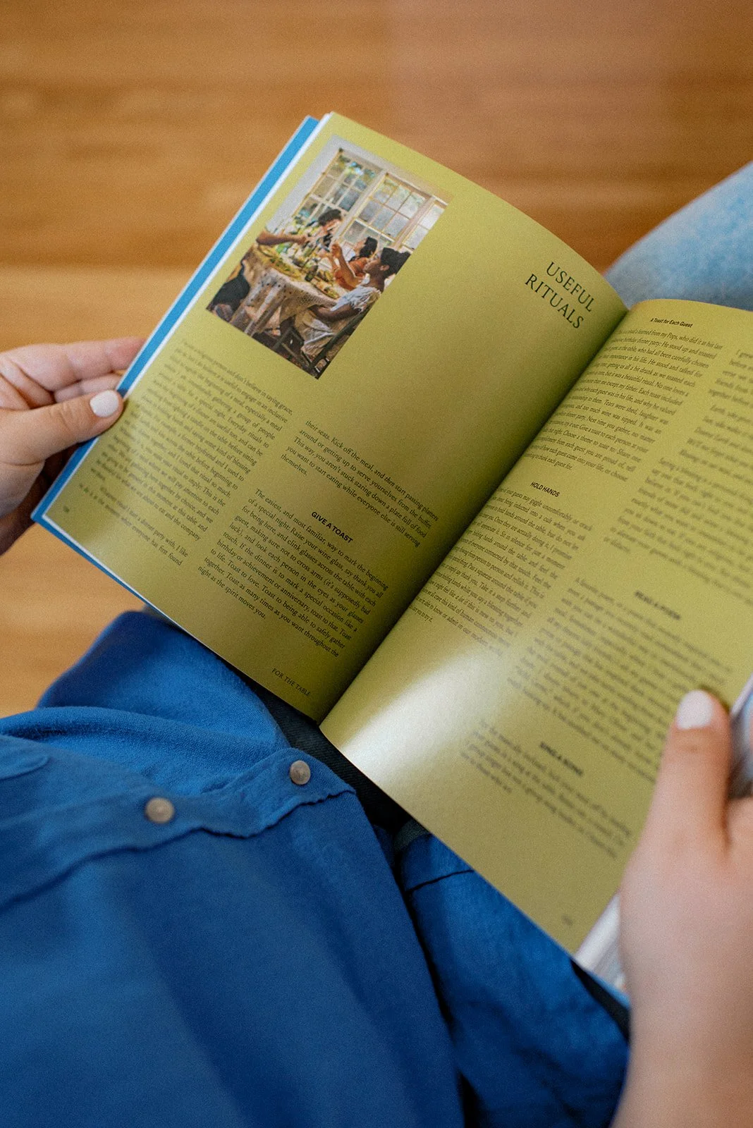 A person sitting on a wooden floor reading a magazine with an article titled 'Useful Rituals' and a photo of people having a meal together at a table by a window.