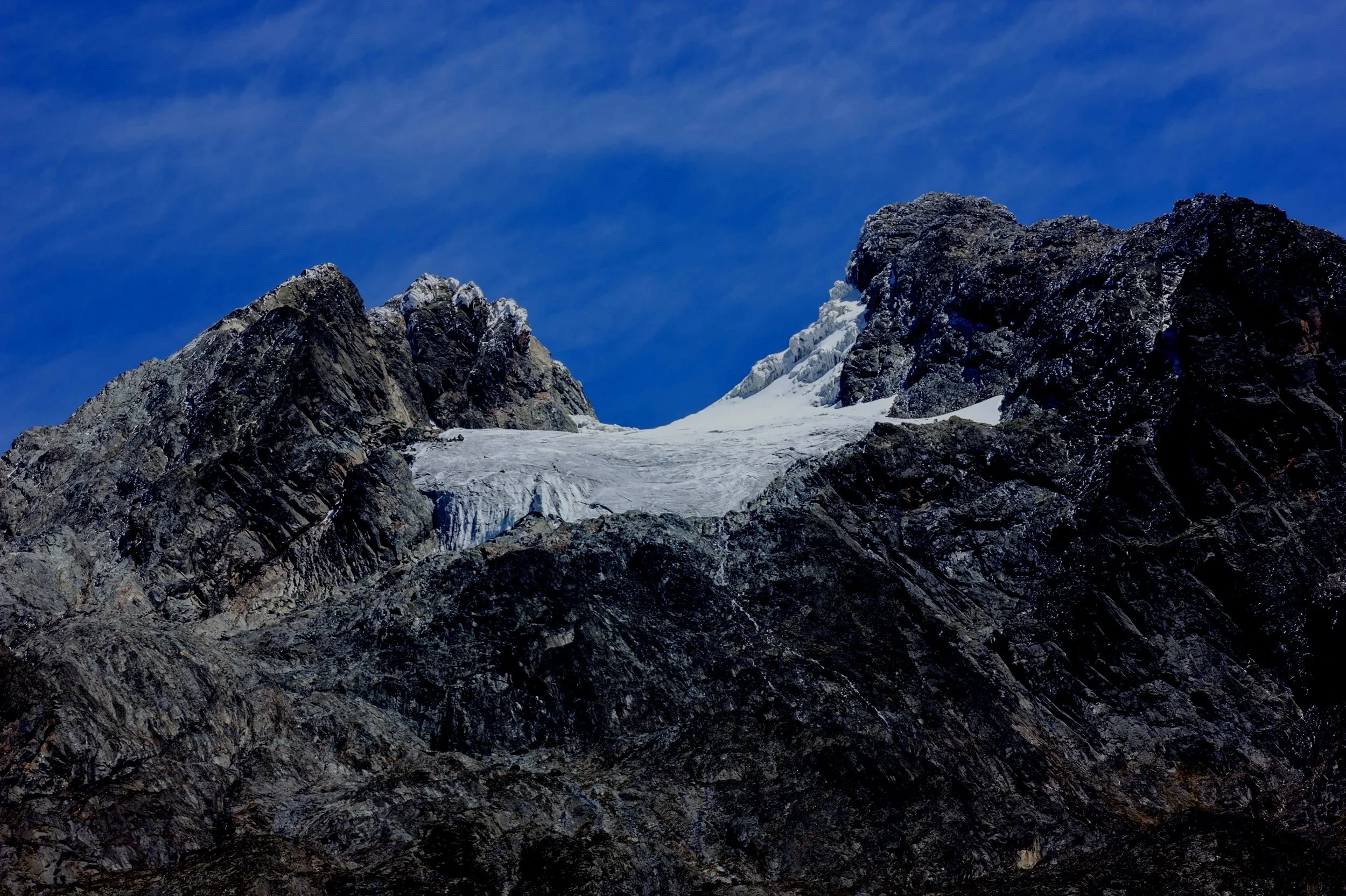 Snow-capped mountain peaks under a clear blue sky with wispy clouds.