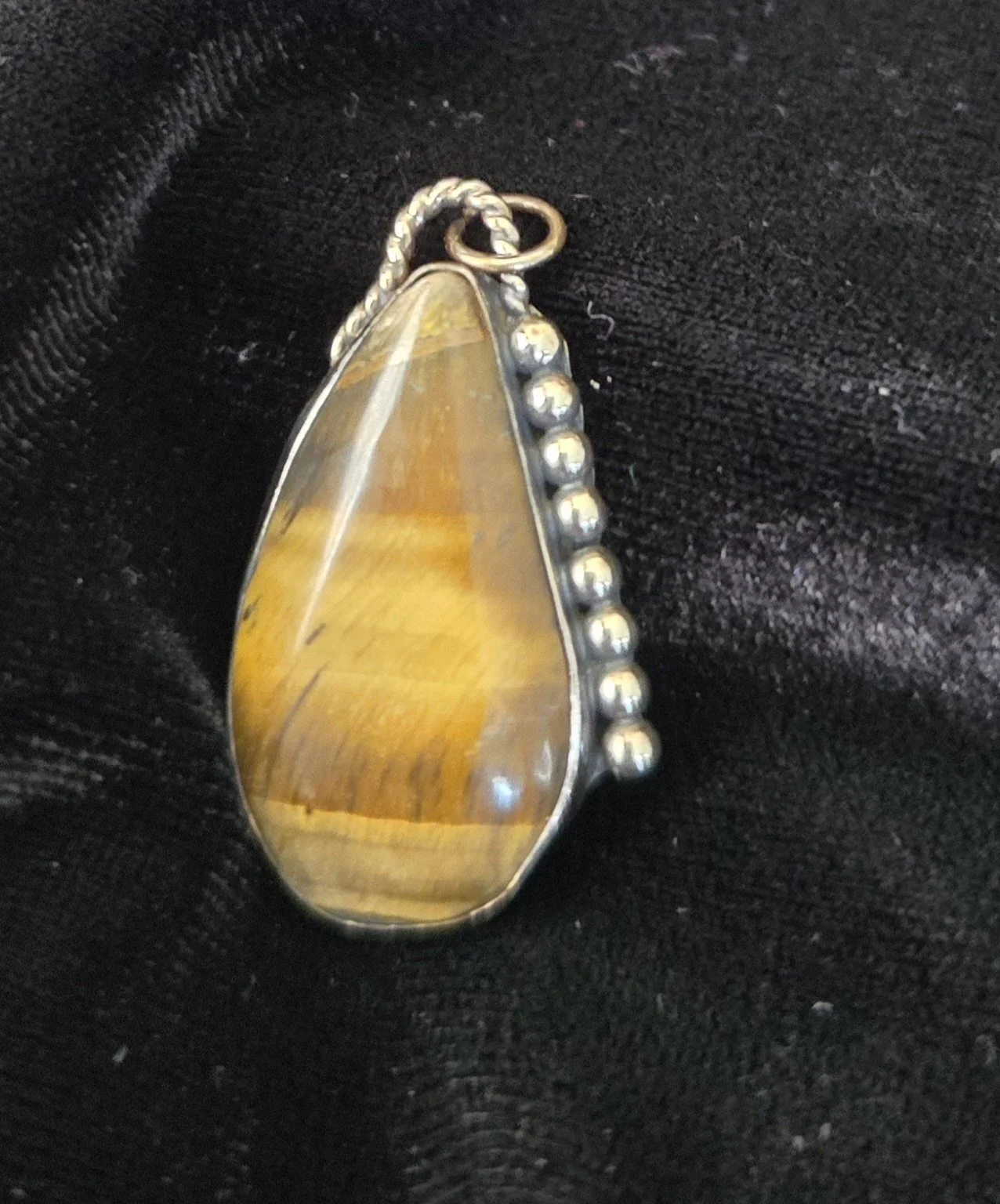 Silver pendant with a teardrop-shaped yellow and brown stone, surrounded by small silver beads, on black fabric
