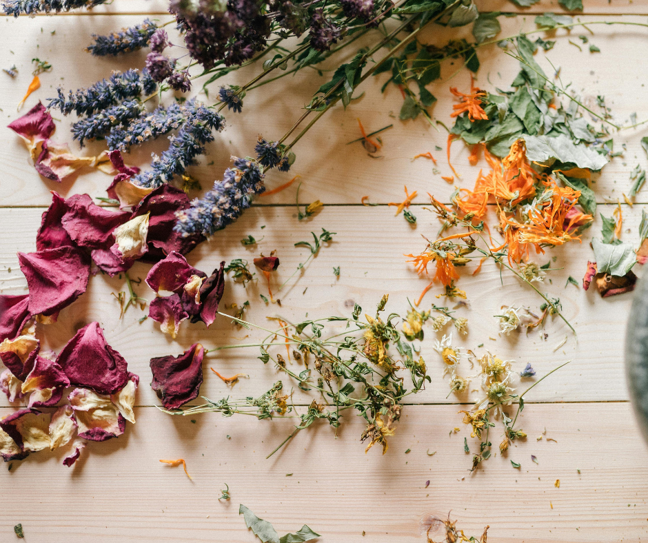 Various dried flowers and flower petals scattered on a light wooden surface.