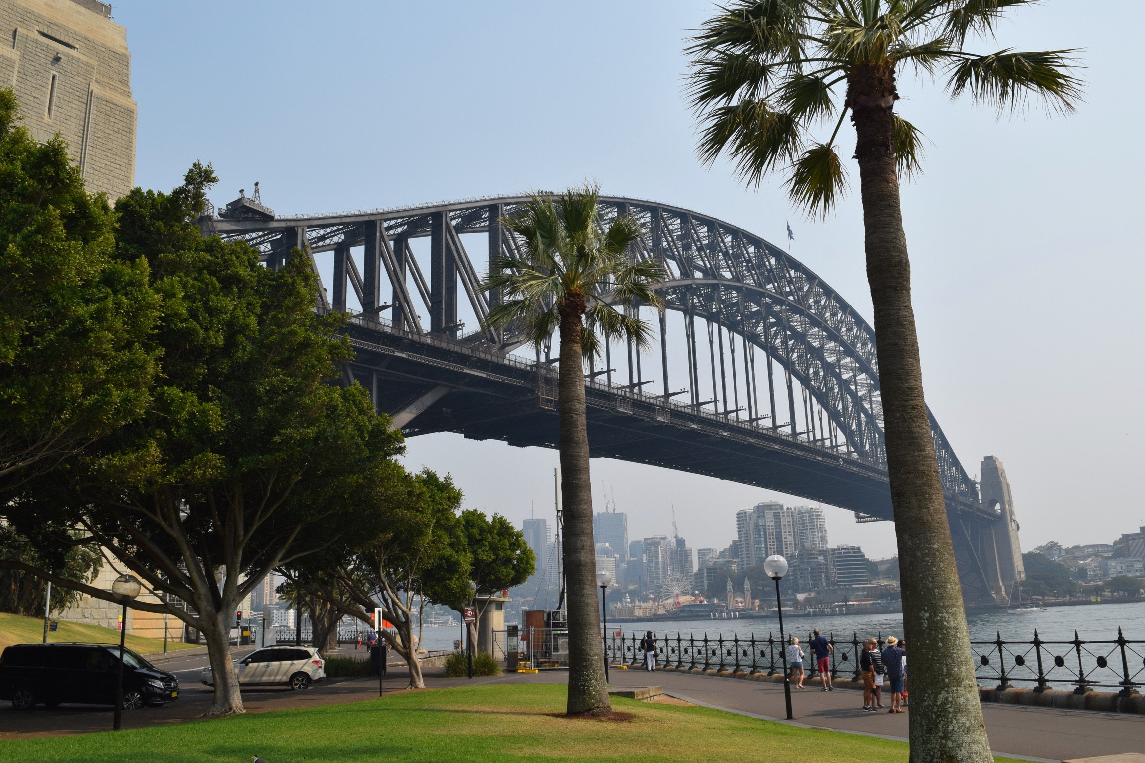 View of the Sydney Harbour Bridge in Australia with trees and people walking along the waterfront park.