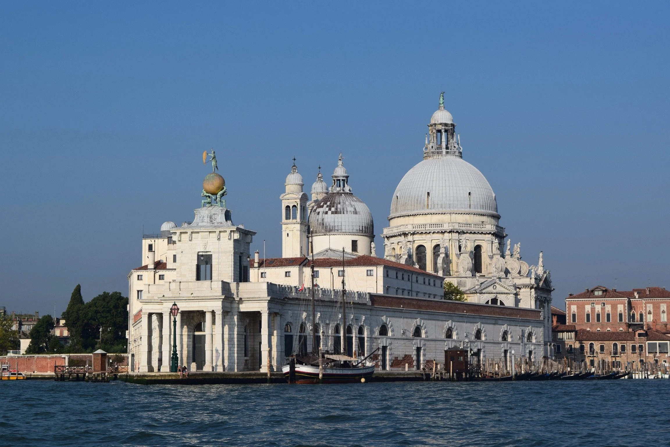 Photo of a historic cityscape with prominent domed basilica, waterfront, and boats, likely Venice, Italy.