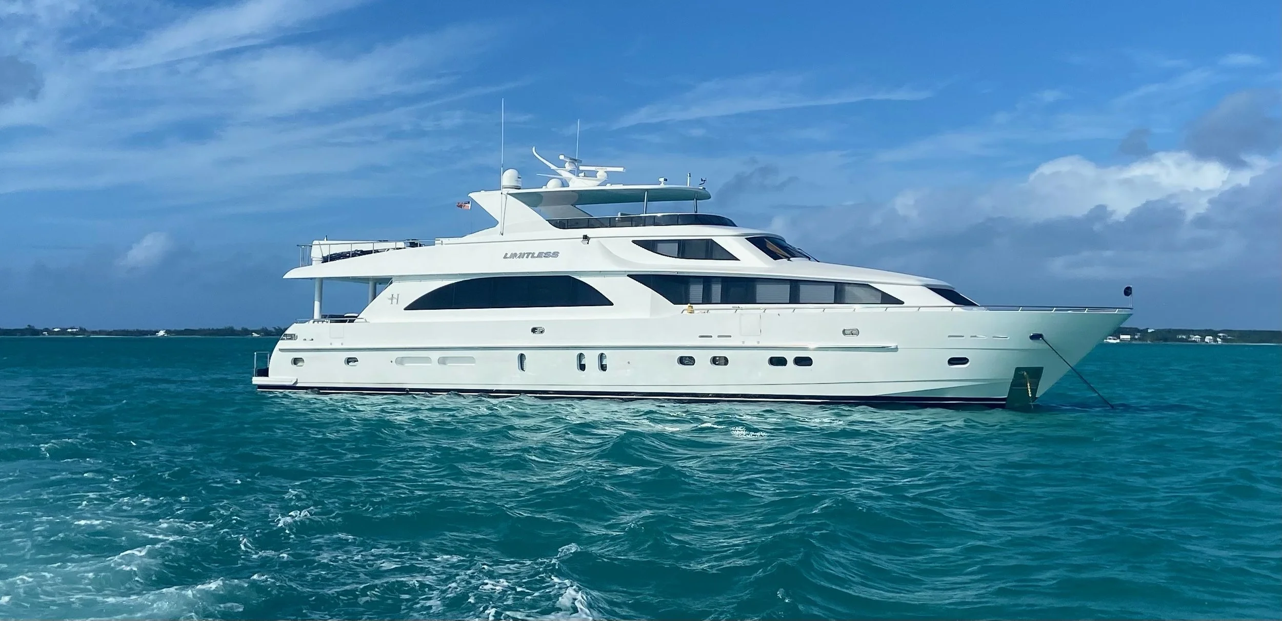 A large white luxury yacht floating on turquoise ocean water under a partly cloudy sky.