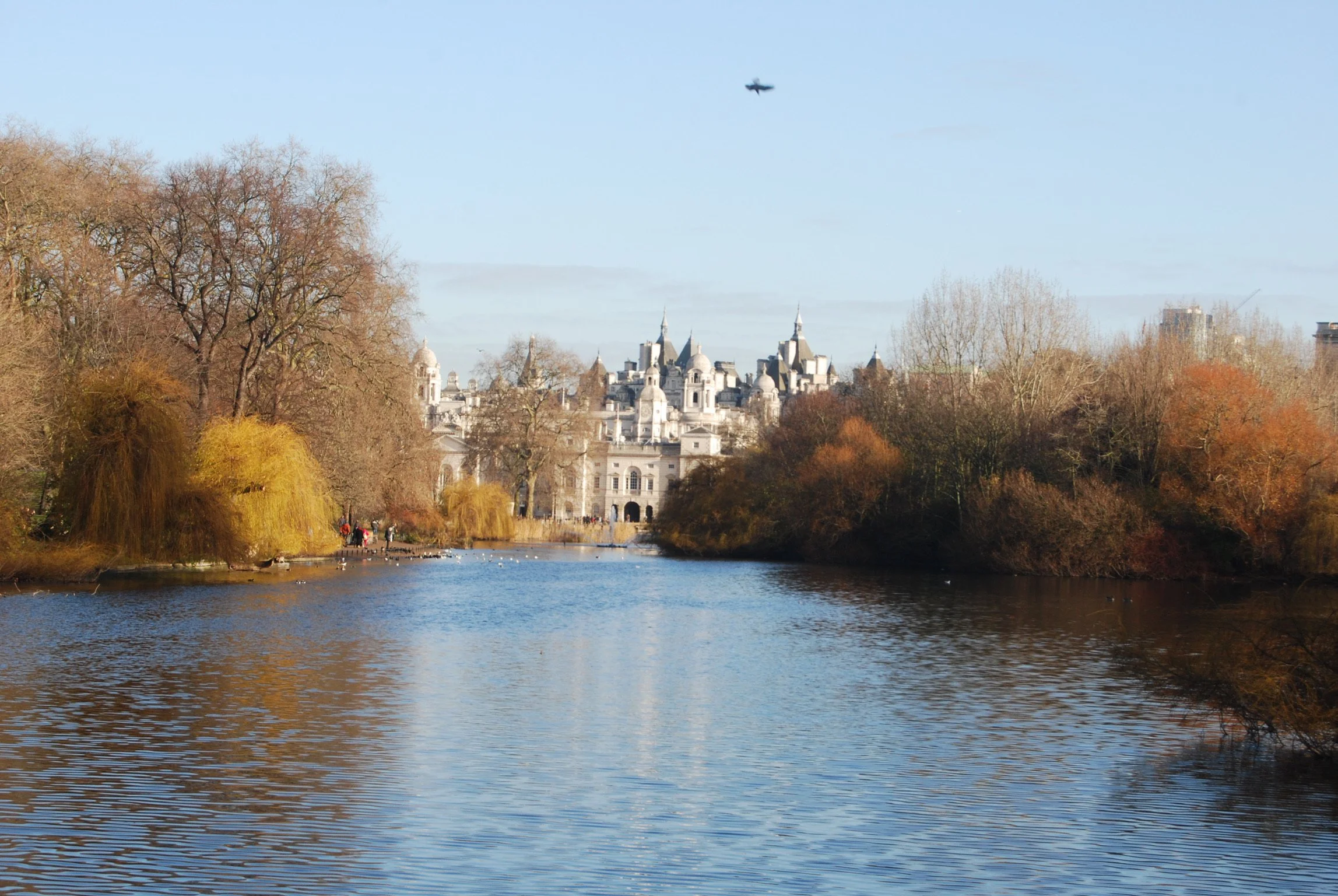 A river with trees on both sides leading to a historic castle in the distance, with a small airplane flying in the clear blue sky.
