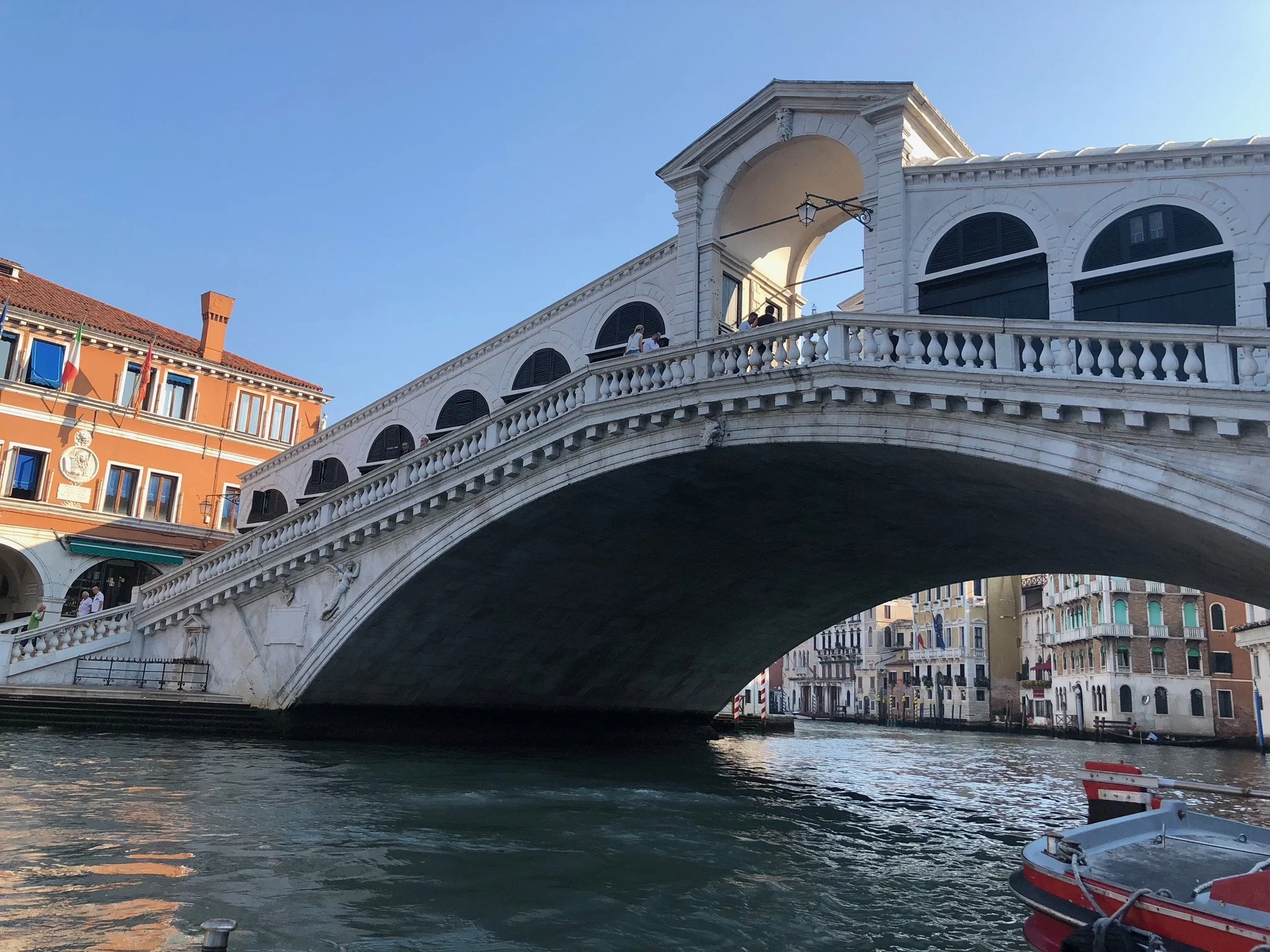 View of the Rialto Bridge over the Grand Canal in Venice, Italy, with surrounding historic buildings and a boat in the water.