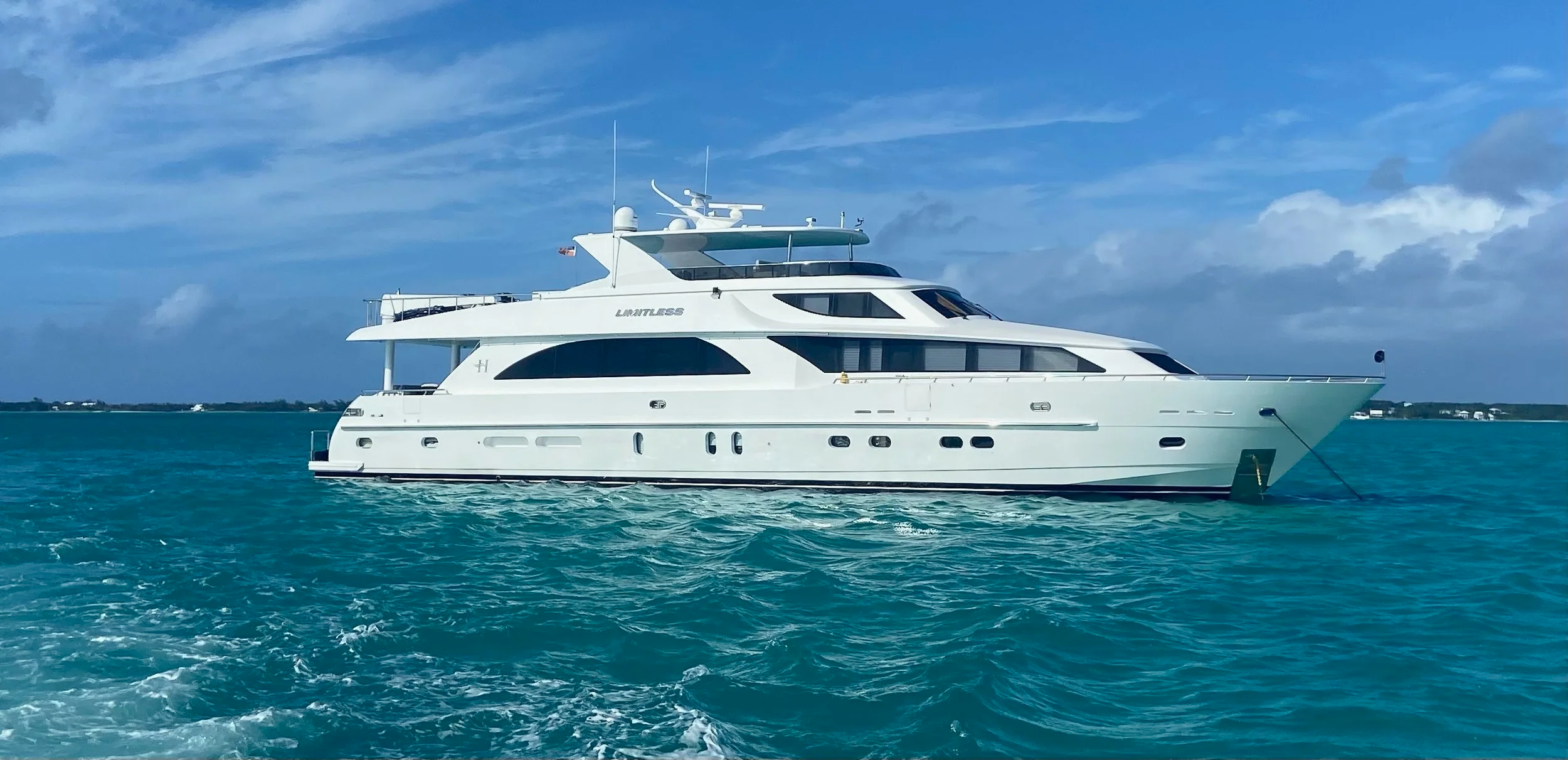 White luxury yacht on turquoise water under a partly cloudy sky with land visible in the background.