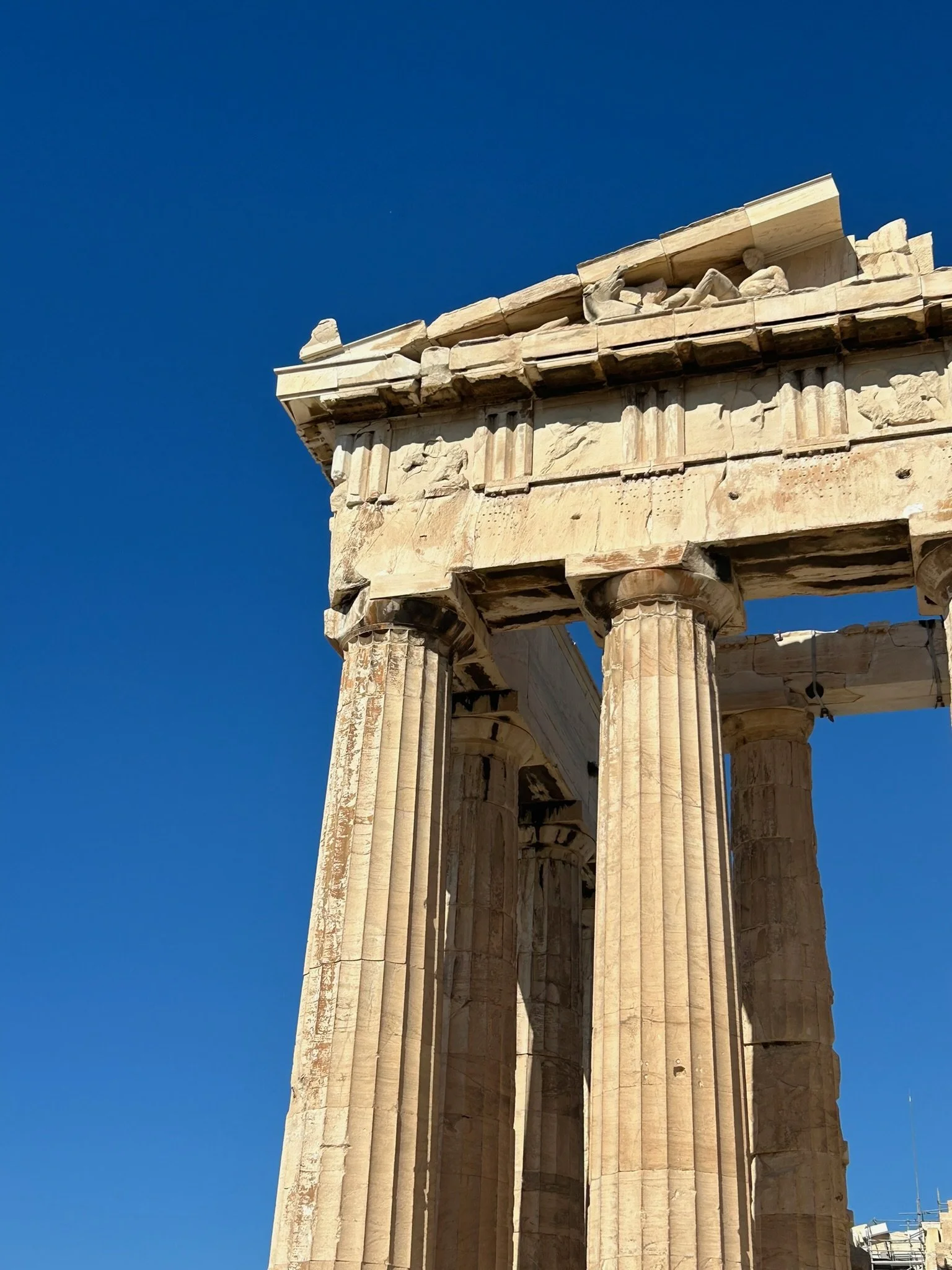 Close-up of ancient Greek ruins with tall, fluted columns under a clear blue sky.
