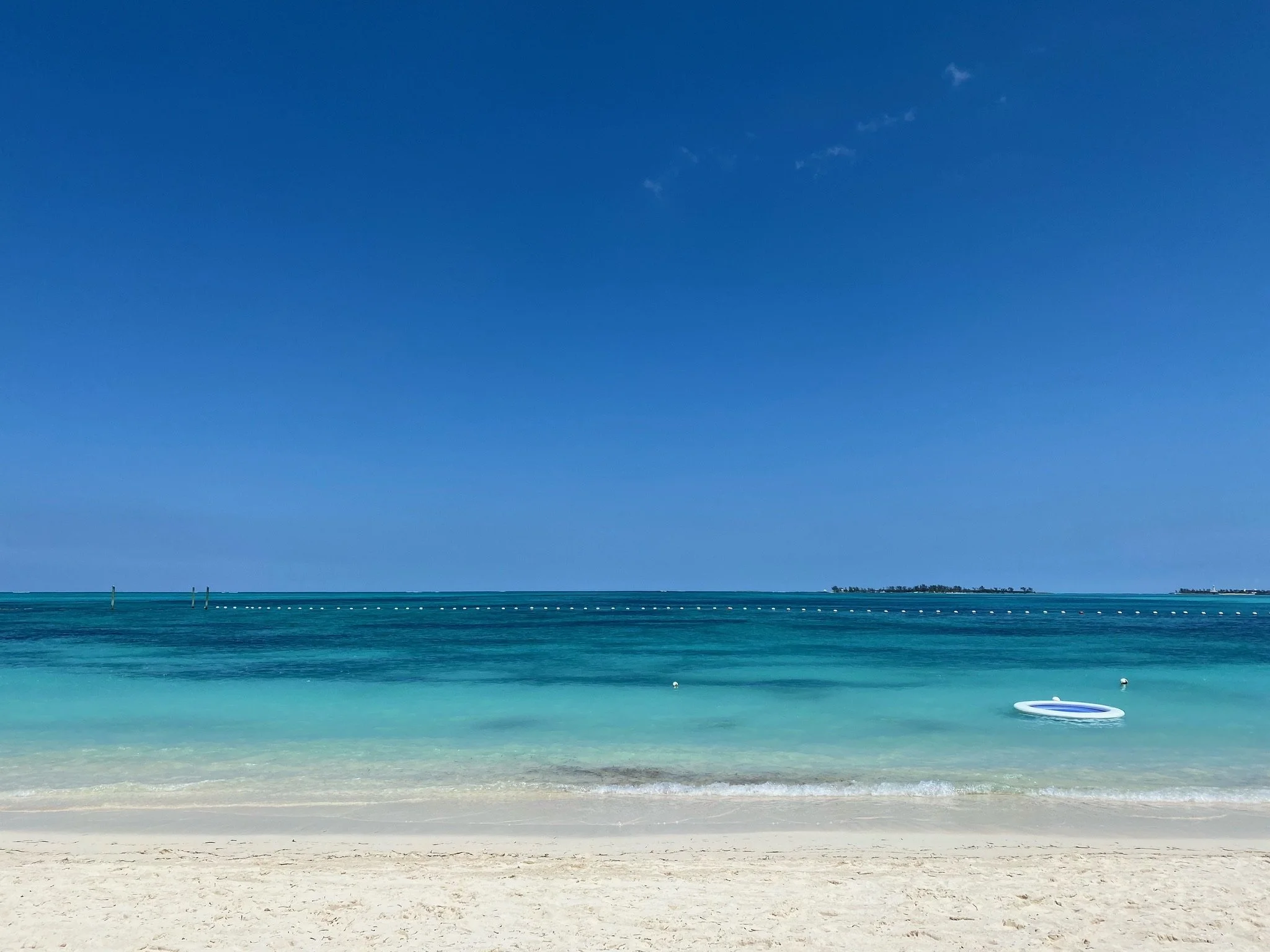 Sunny beach with white sand, turquoise water, and a clear blue sky, with a small inflatable boat floating near the shore.