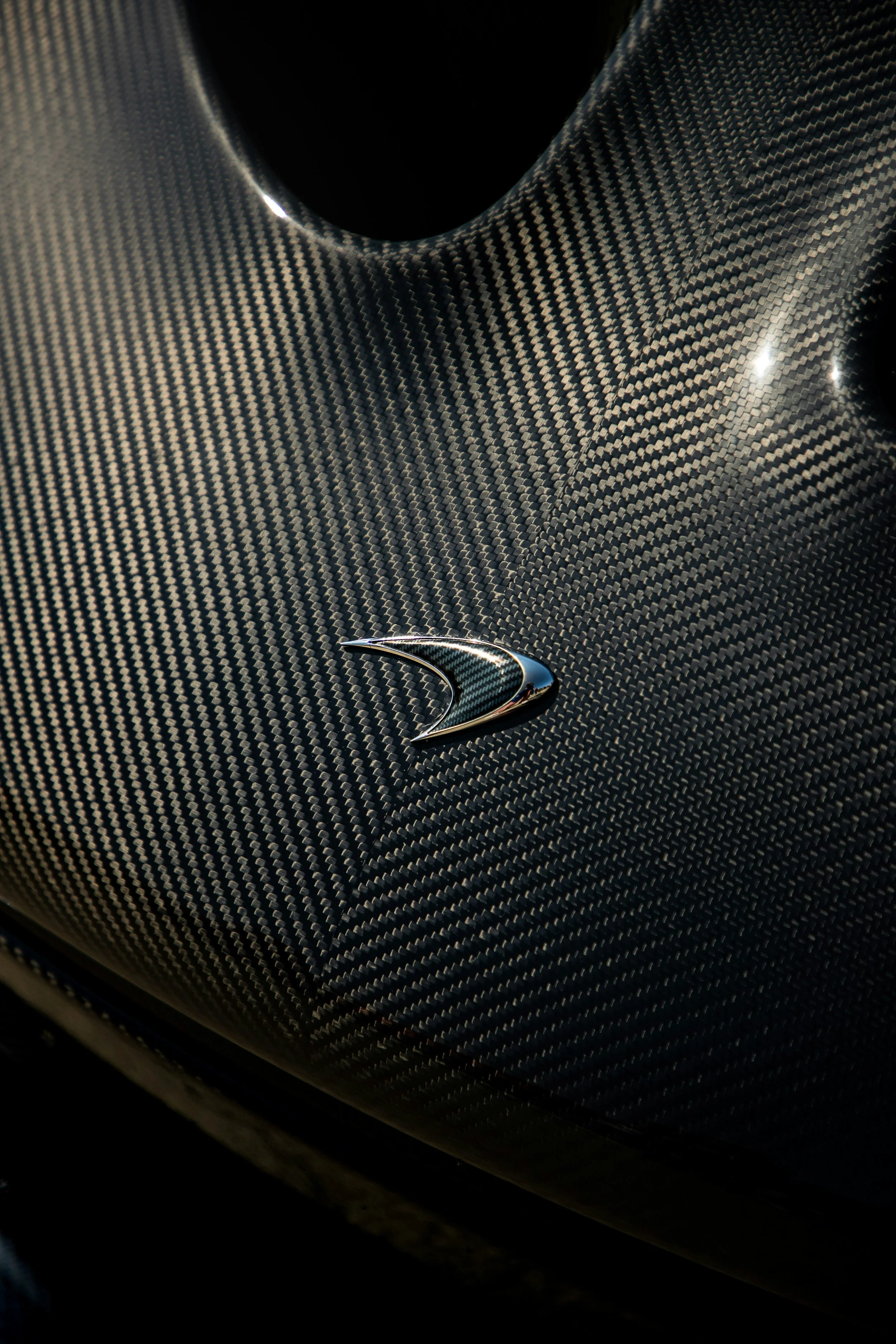 Close-up of a car's hood covered in carbon fiber material, featuring a metallic emblem.