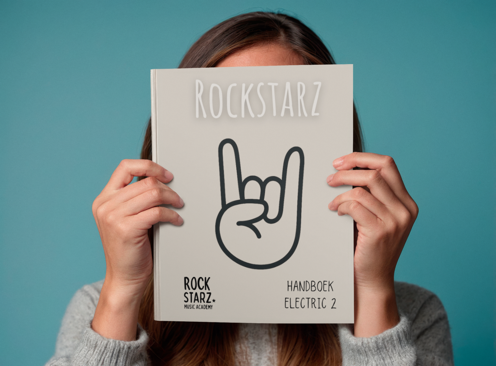 Person holding a music book titled 'Rockstarz' in front of their face, the cover features a hand making a rock and roll gesture and the words 'Handboek Electric 2' and 'Rockstarz' at the bottom.