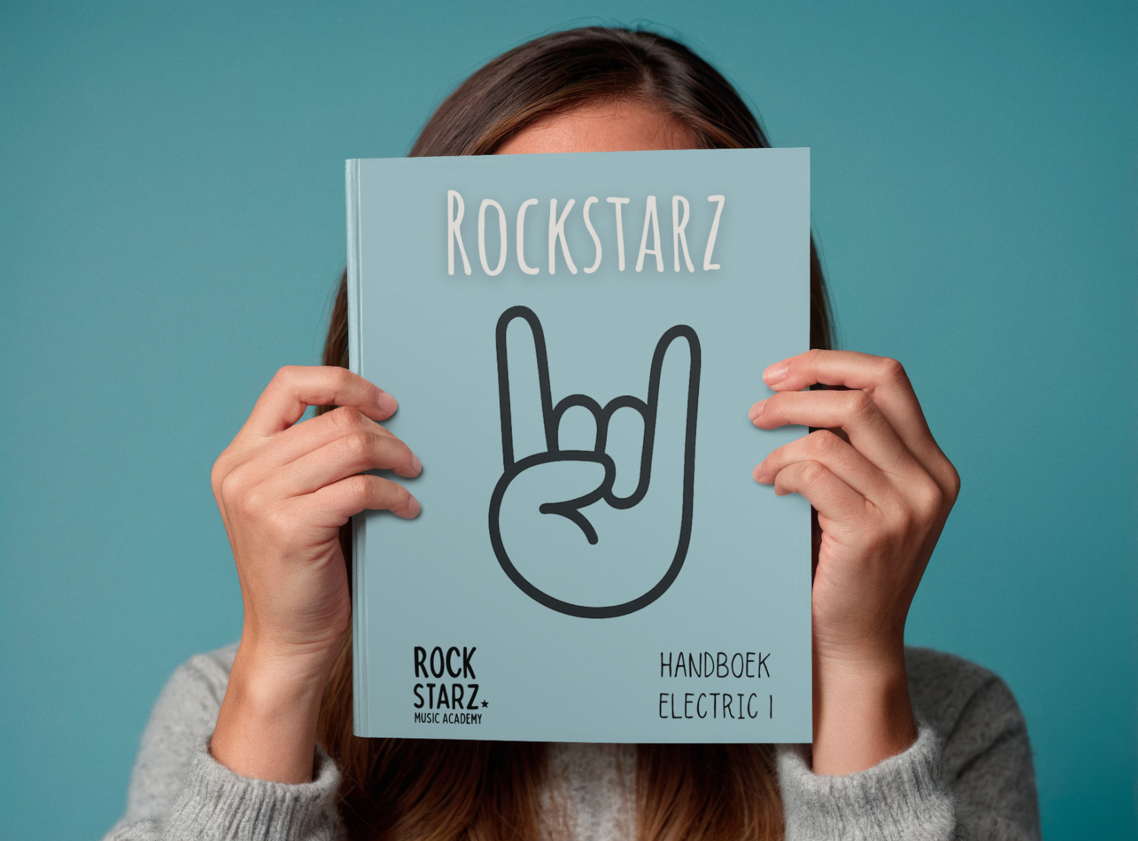Person holding a blue music handbook titled "Rockstarz" in front of their face, with a hand making the rock and roll gesture, against a blue background.
