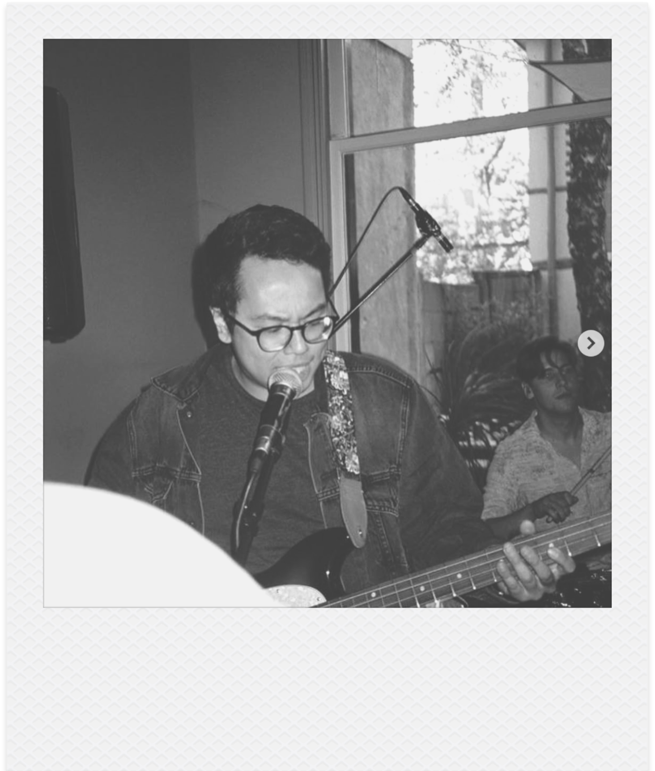 Een man met bril die zingt door een microfoon en basgitaar speelt.