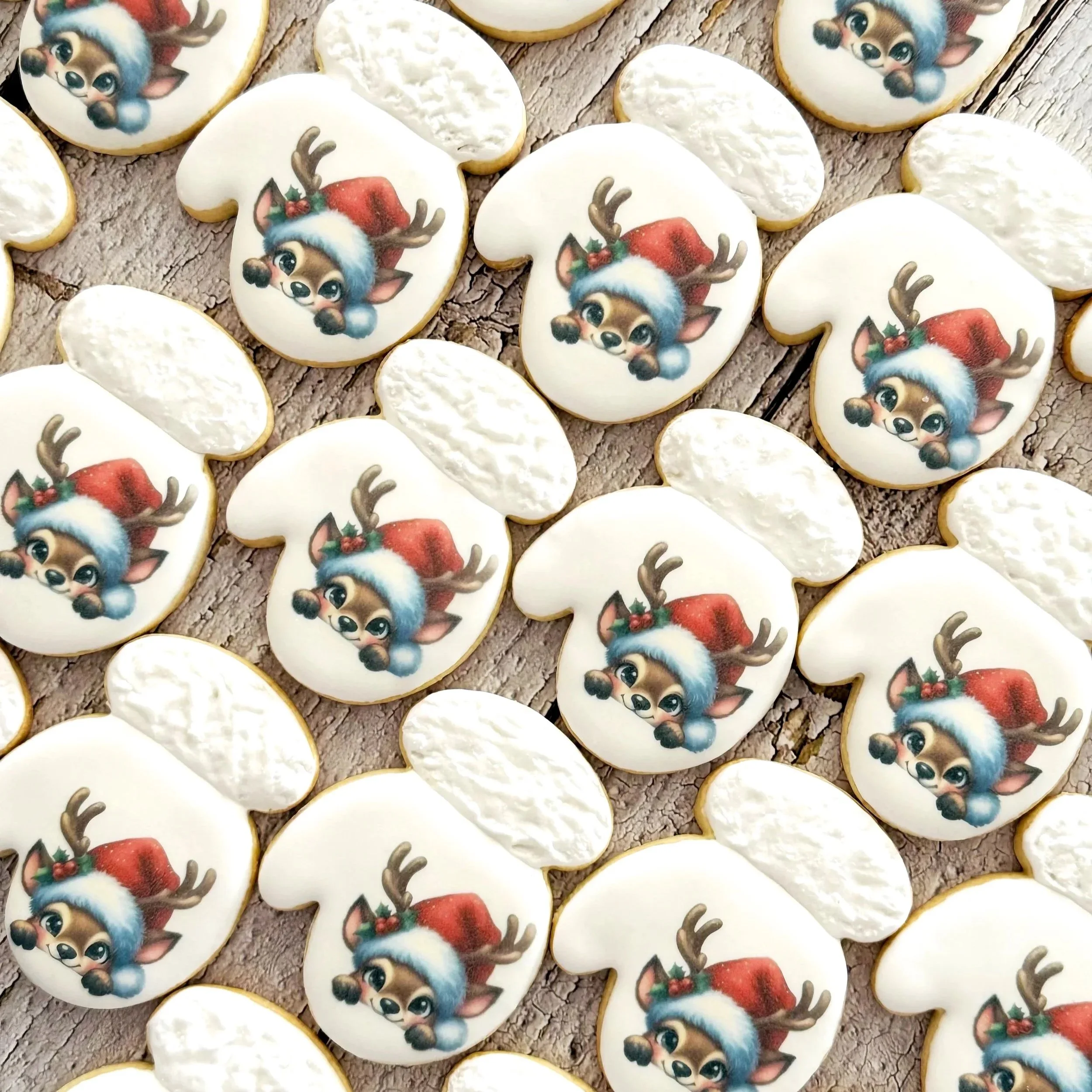 Decorated Christmas cookies shaped like reindeer faces with Santa hats and reindeer antlers, placed on a rustic wooden surface.