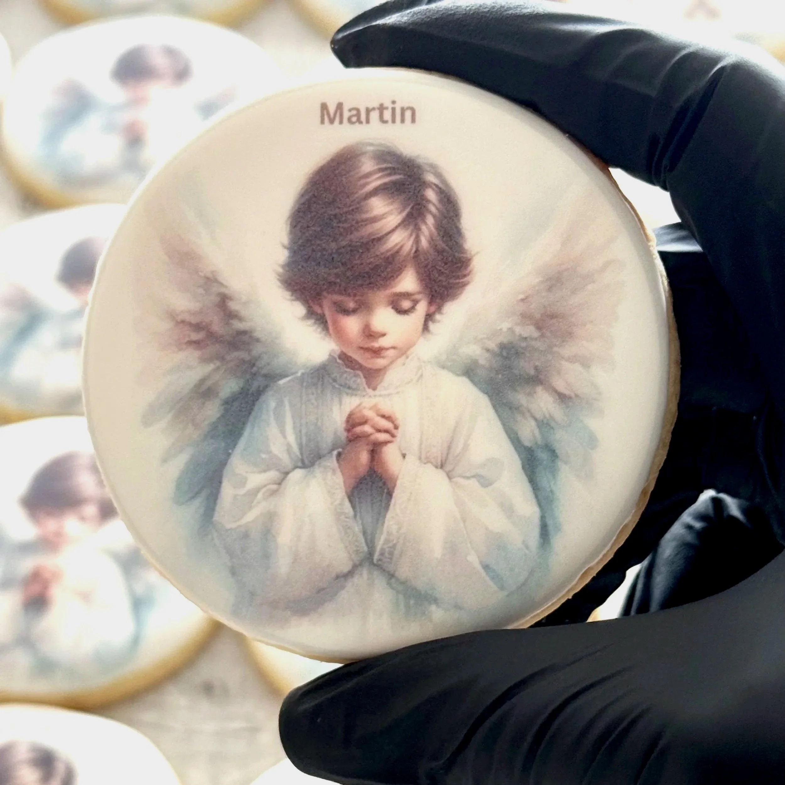 Decorative cookie featuring an illustration of a young angel with praying hands, brown hair, and white wings, with the name 'Martin' printed above.