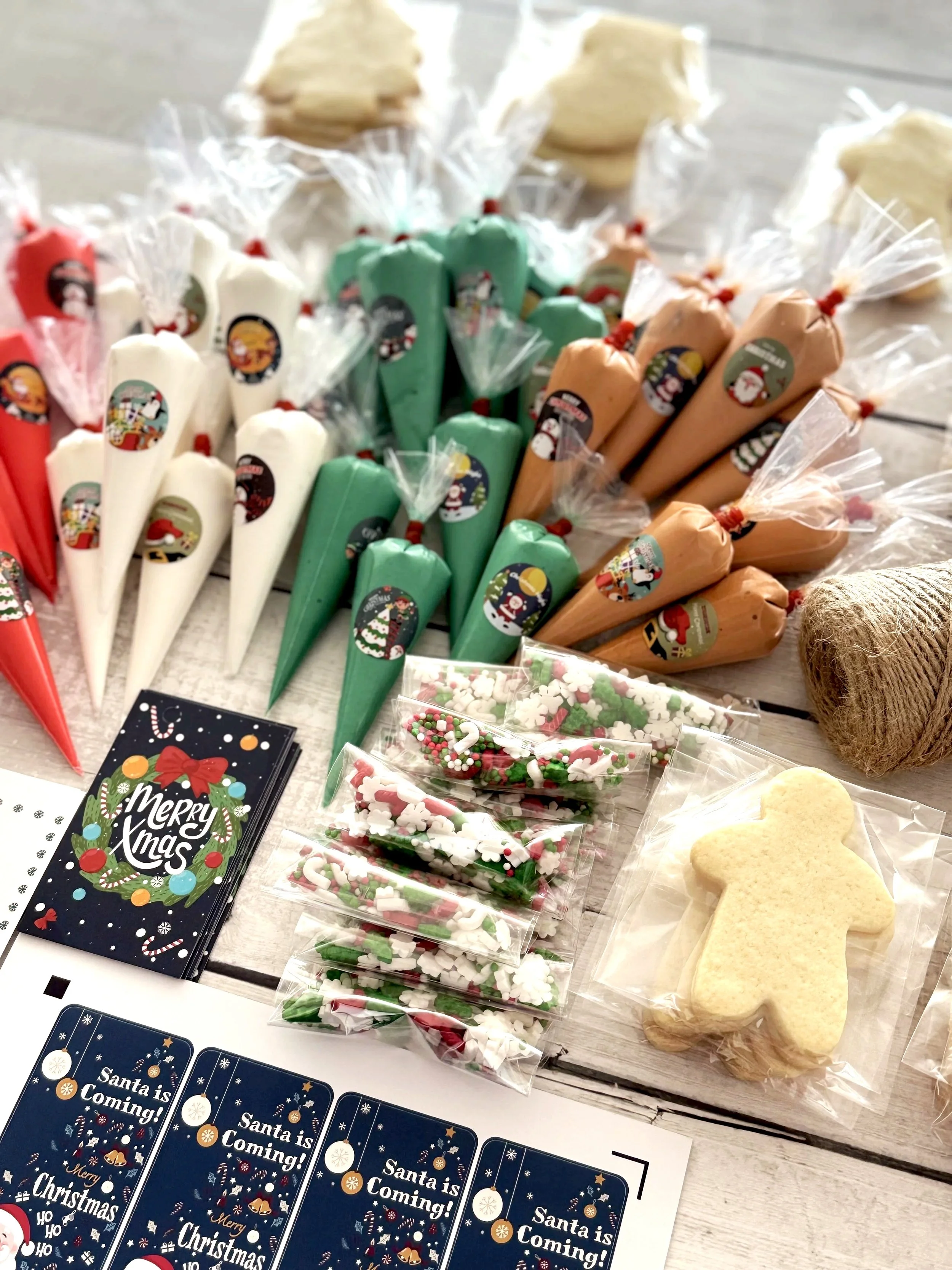 Assorted Christmas-themed cookies and candies, including colorful frosting cones, sugar cookies, and holiday stickers, displayed on a wooden surface.