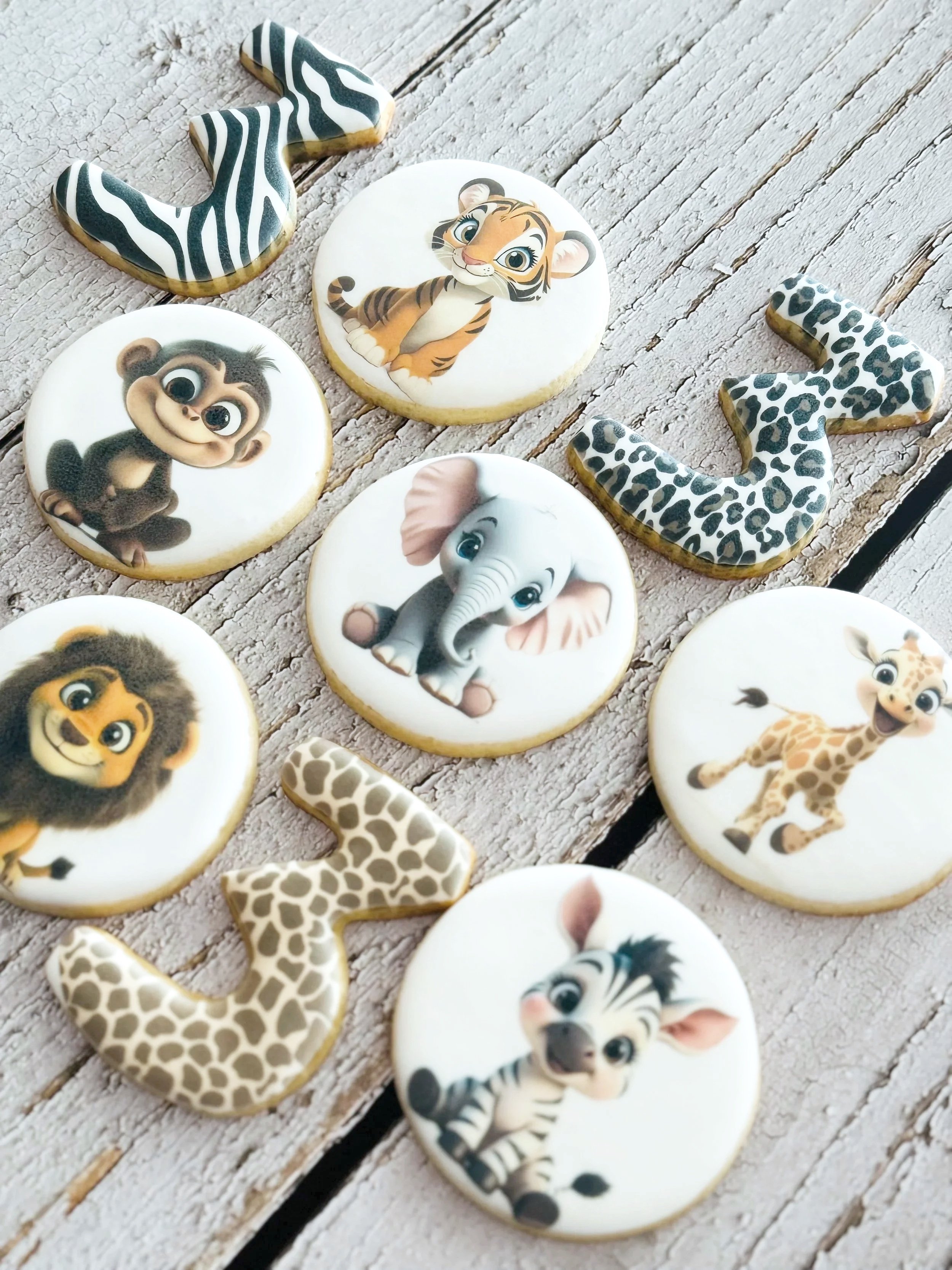 Decorative cookies featuring cartoon animals like a tiger, elephant, zebra, lion, monkey, giraffe, and a zebra, arranged on a wooden surface.