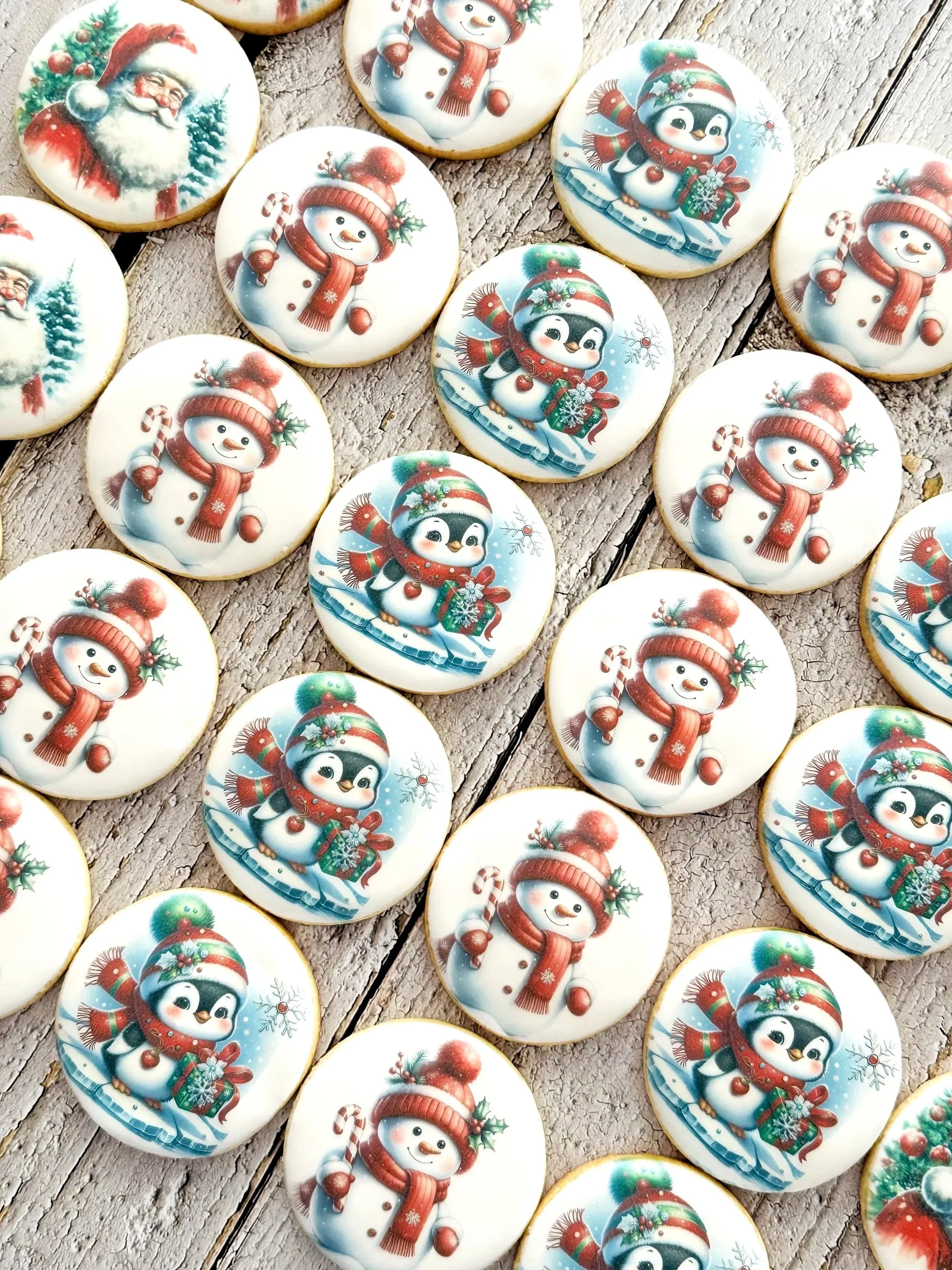 Collection of holiday cookies decorated with images of Santa Claus, snowmen, and penguins wearing winter hats and scarves, on a rustic wooden surface.