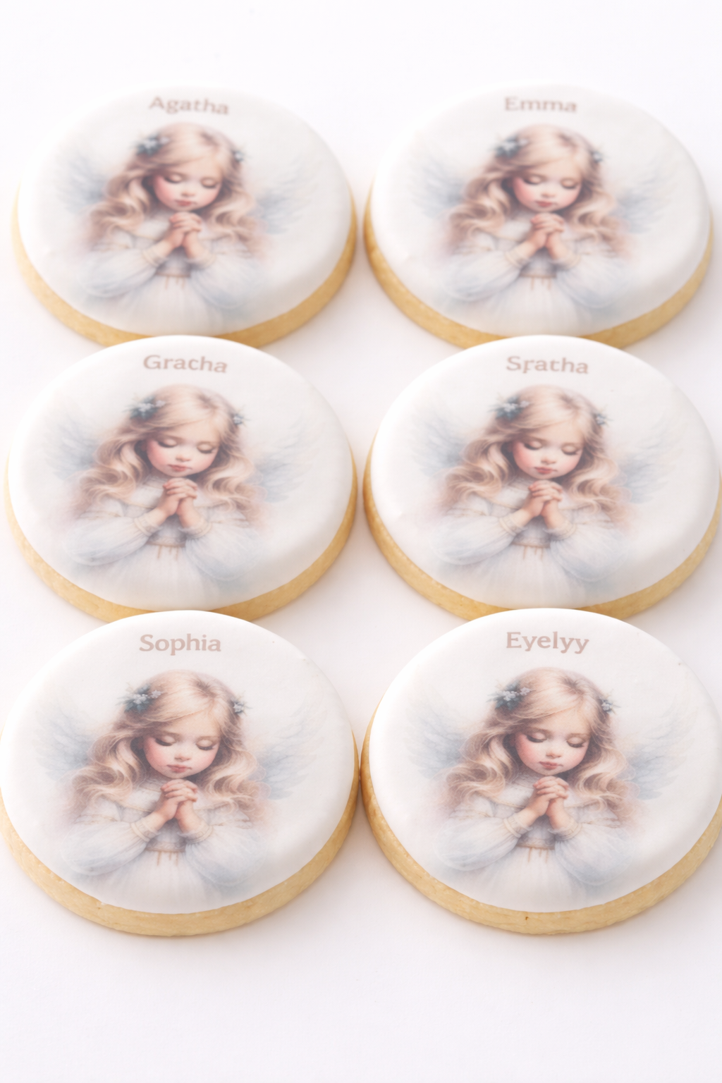 Cookies decorated with an image of a young girl with long blonde hair, praying with hands clasped, on a white background, with names "Agatha" and "Gracia" inscribed on some cookies.