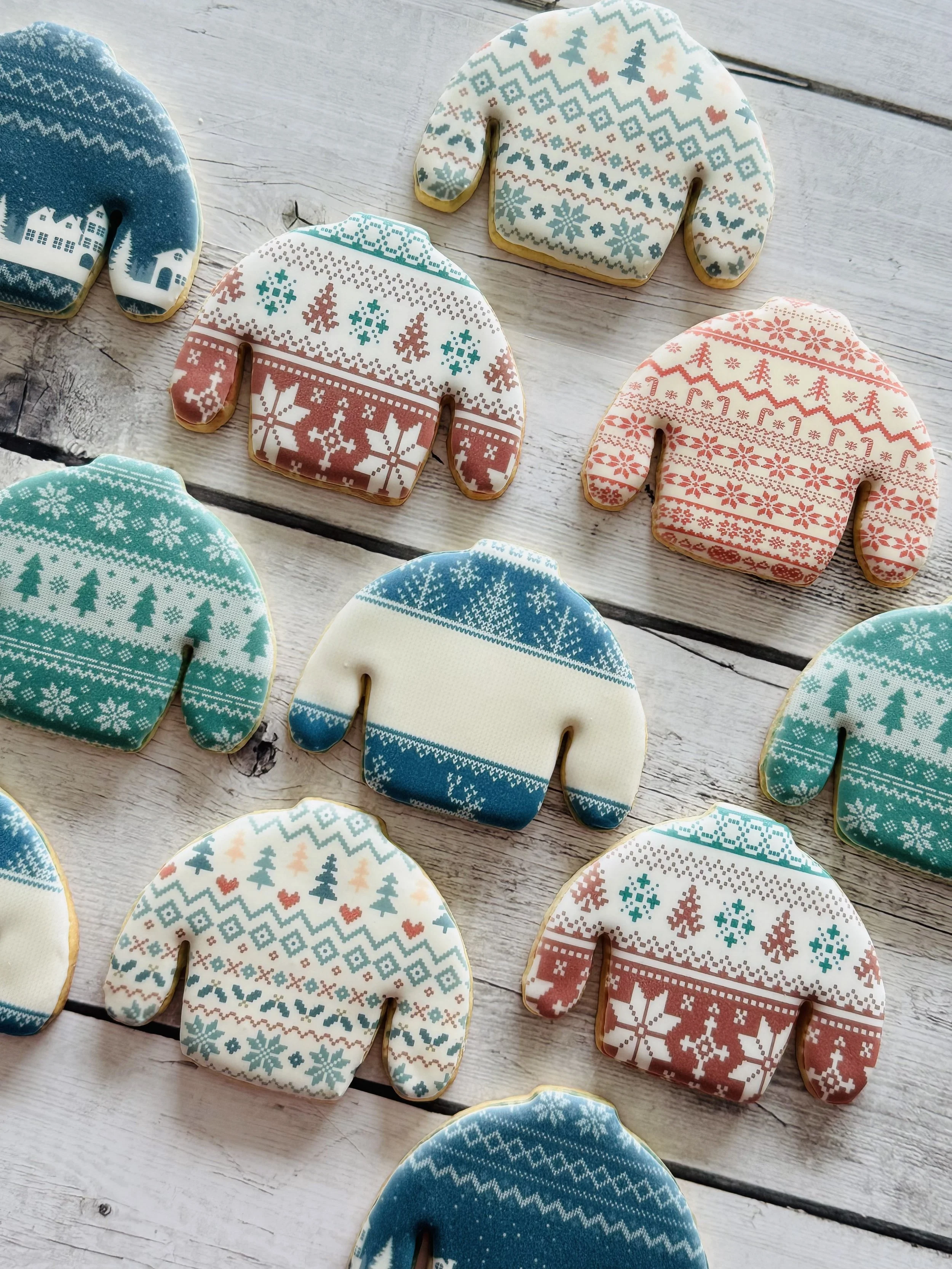 Assorted decorated Christmas cookies shaped like mittens with various festive patterns laid on a white wooden surface.