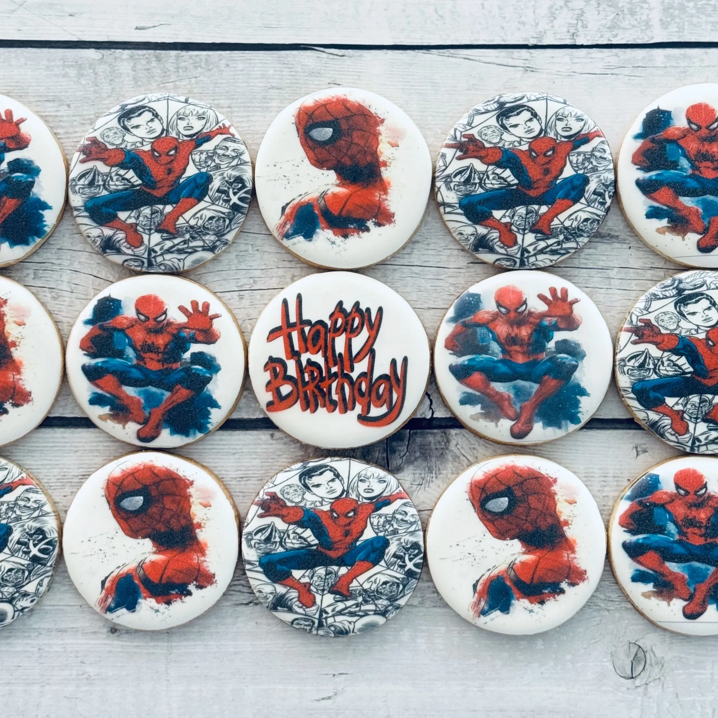 Collection of Spider-Man themed birthday cookies with various Spider-Man images and a cookie with the message "Happy Birthday" written on it, all placed on a light wooden surface.