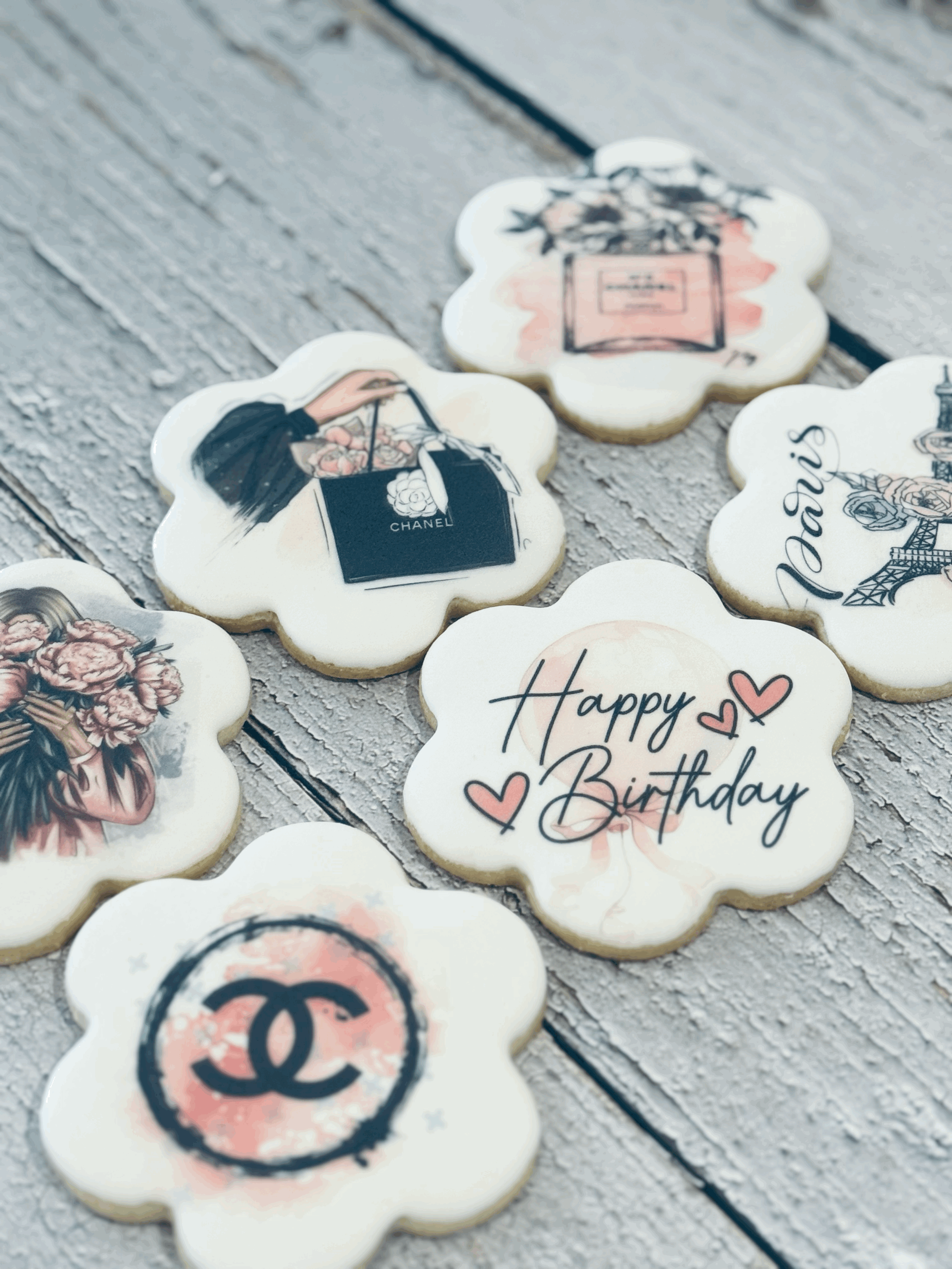 Decorative cookies with fashion and luxury brand logos and messages, including a "Happy Birthday" message with hearts, on a rustic wooden surface.