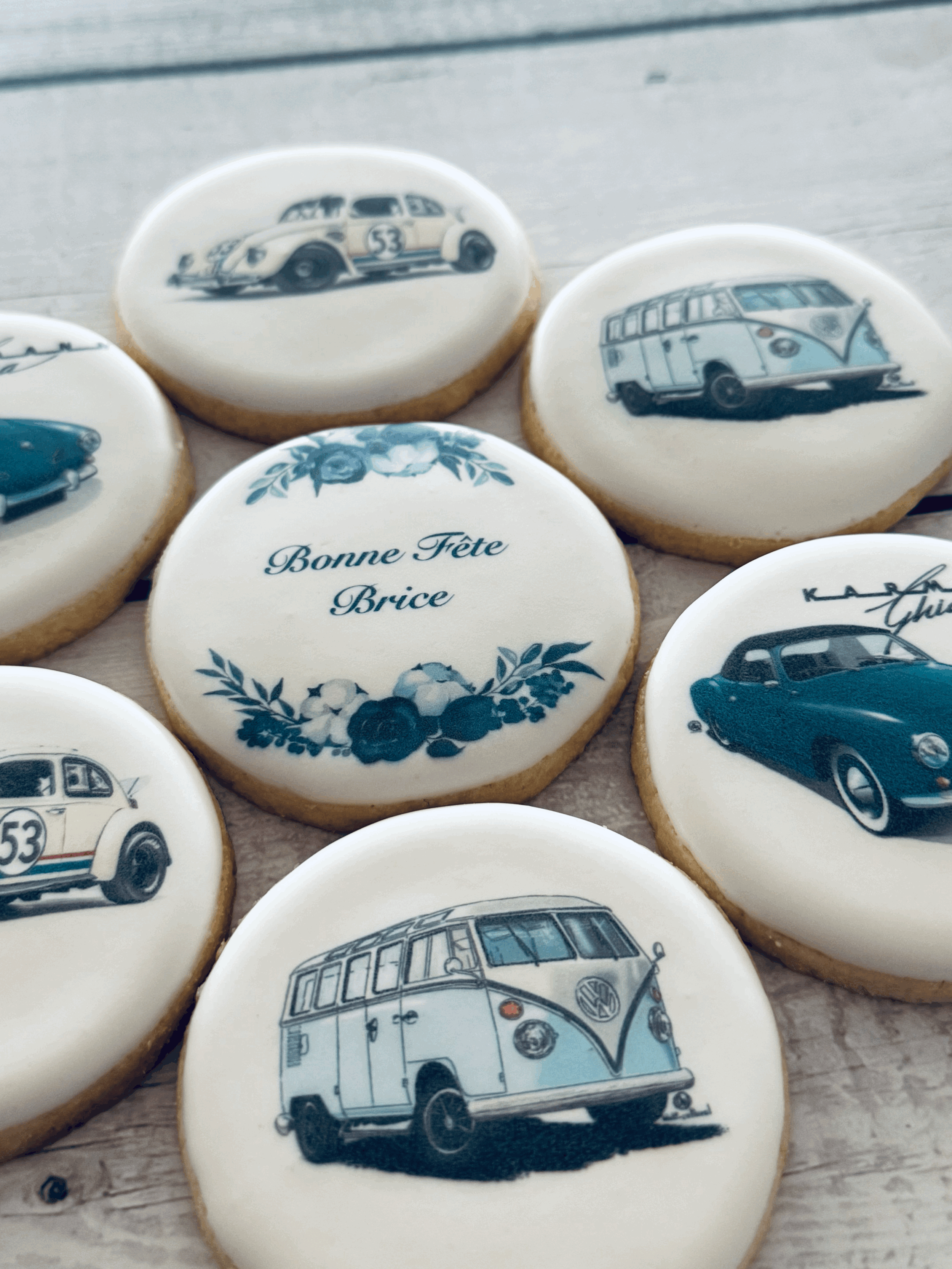 Cookies decorated with images of vintage cars, including a Porsche 911, a Volkswagen Type 2, and a classic Mini, along with a cookie with French text 'Bonne Fête Brice' and floral illustrations.