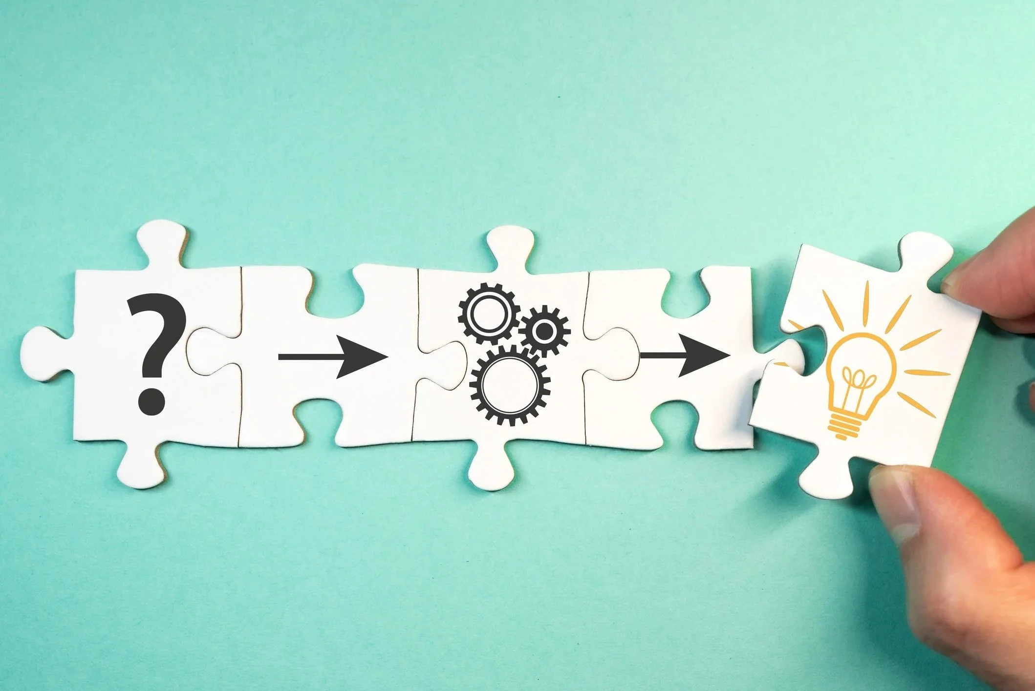 Puzzle pieces with symbols representing a question mark, arrow, gears, and a lightbulb on a light blue background, illustrating a process of problem solving and idea generation.
