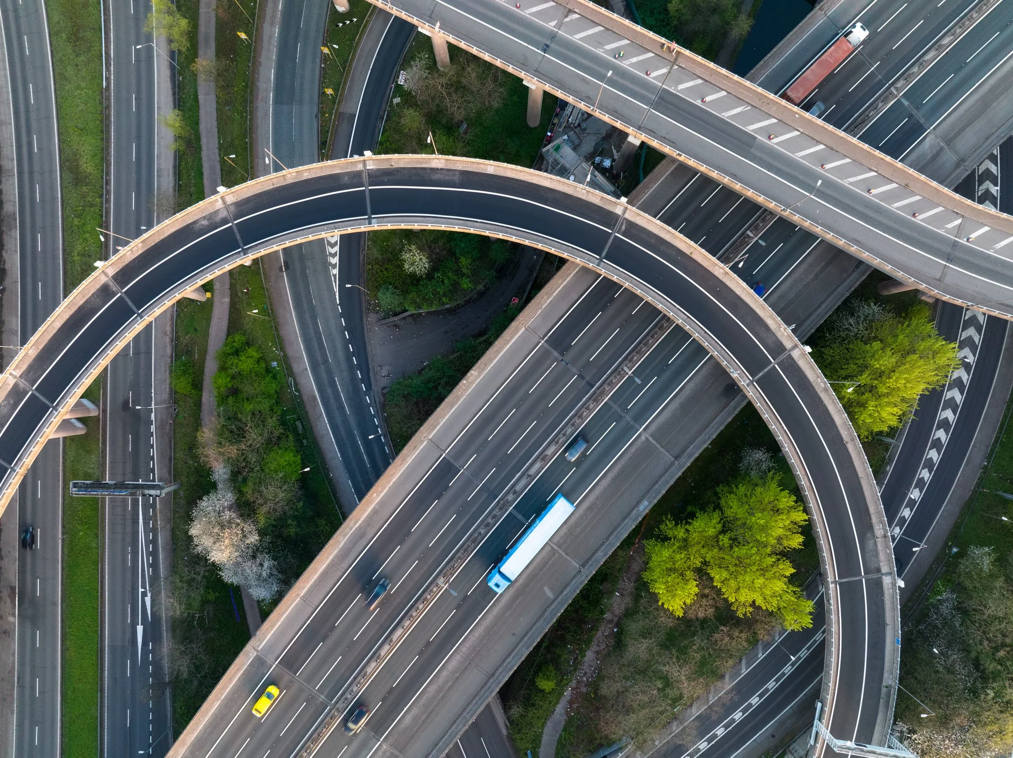 An aerial view of a complex highway interchange with multiple roads and overpasses, including a curved ramp and a bridge, surrounded by greenery.