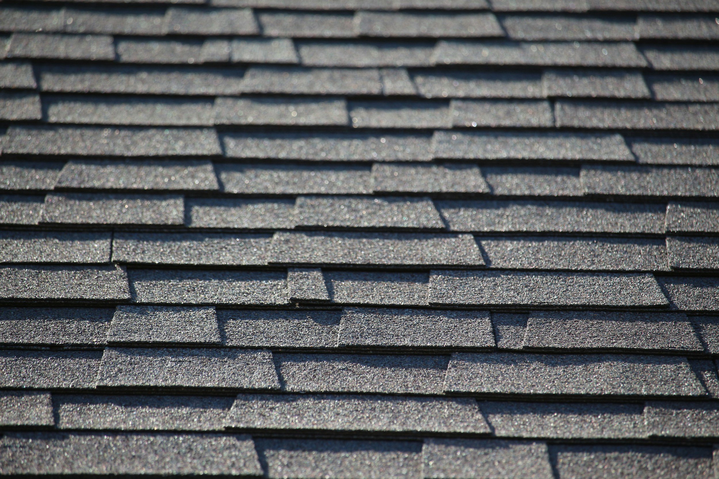 Close-up of dark gray asphalt shingles on a roof with a textured surface and layered overlapping pattern.