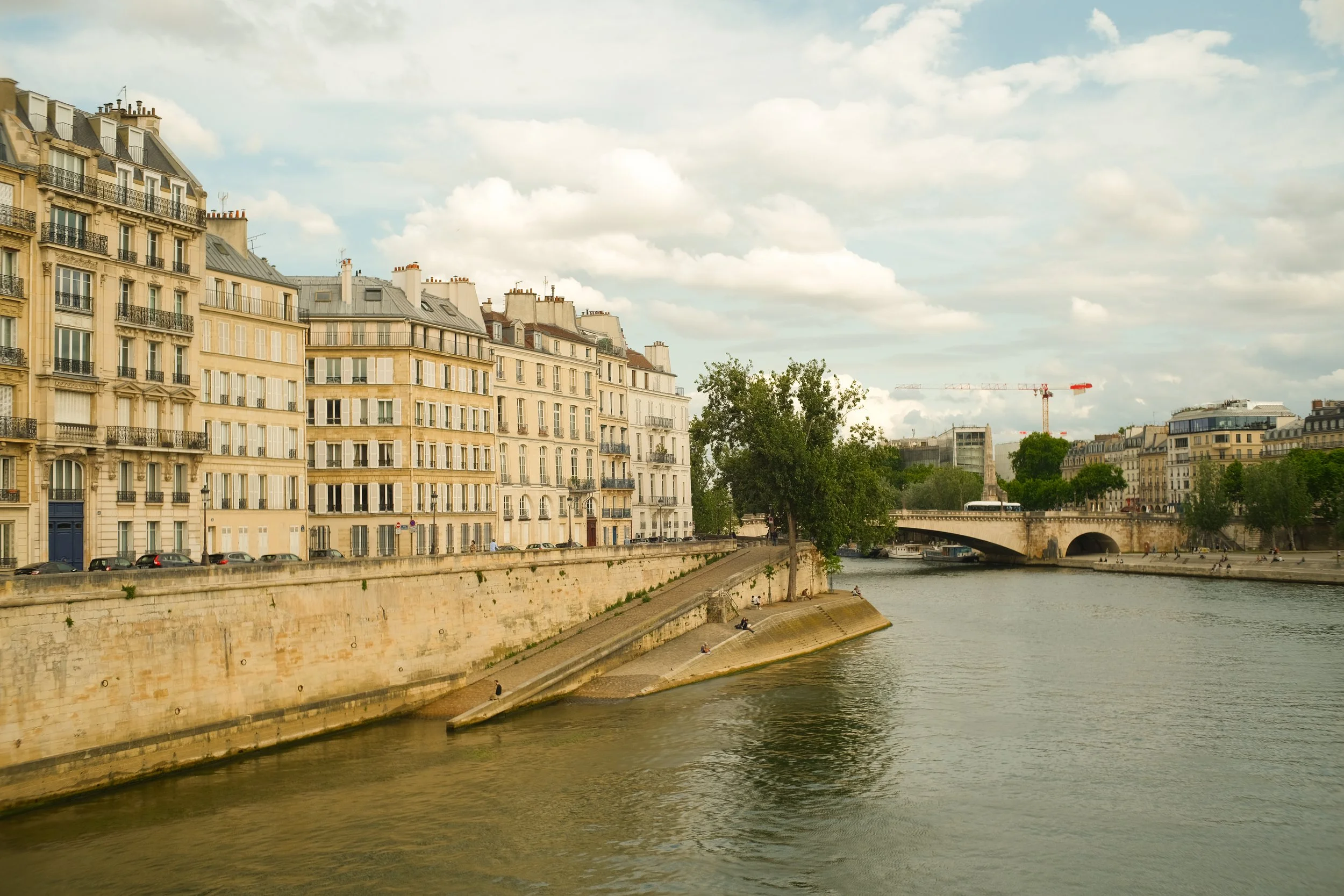 Blick auf die Seine in Paris mit historischen Gebäuden am Ufer, einer Brücke im Hintergrund und einem bewölkten Himmel.