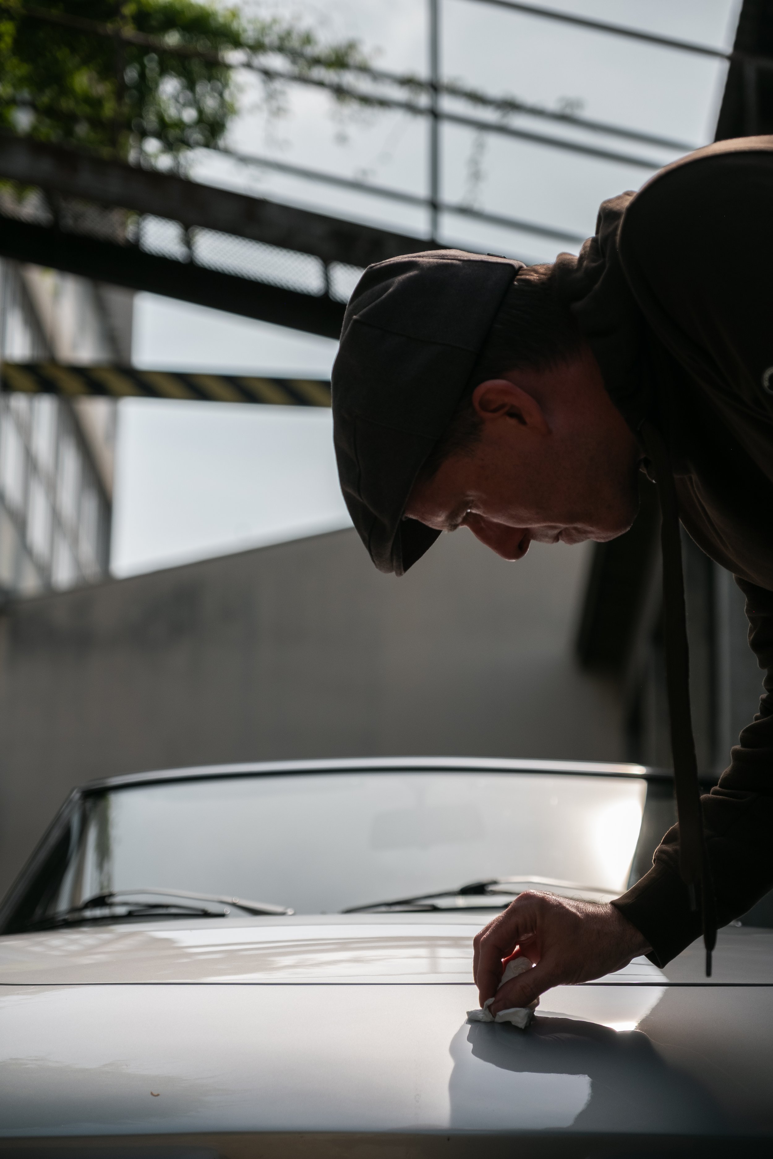 Mann putzt die Motorhaube eines alten Autos mit einem Tuch in einer Garage oder Werkstatt.