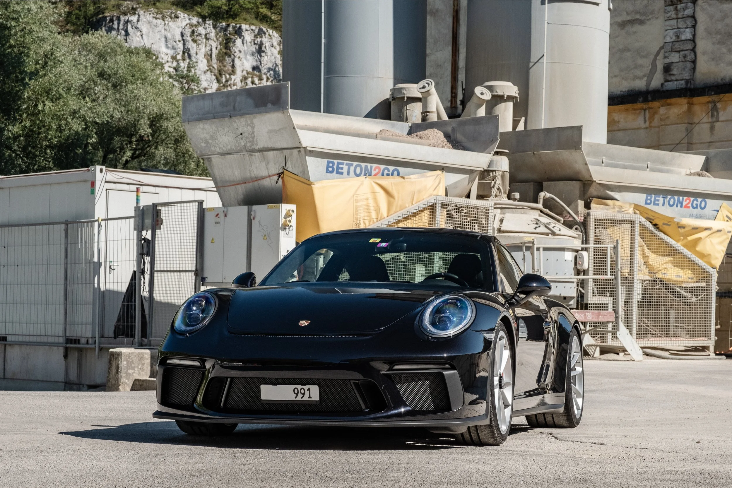 Schwarzer Porsche 911 vor einer Baustelle mit Betonmischmaschinen.