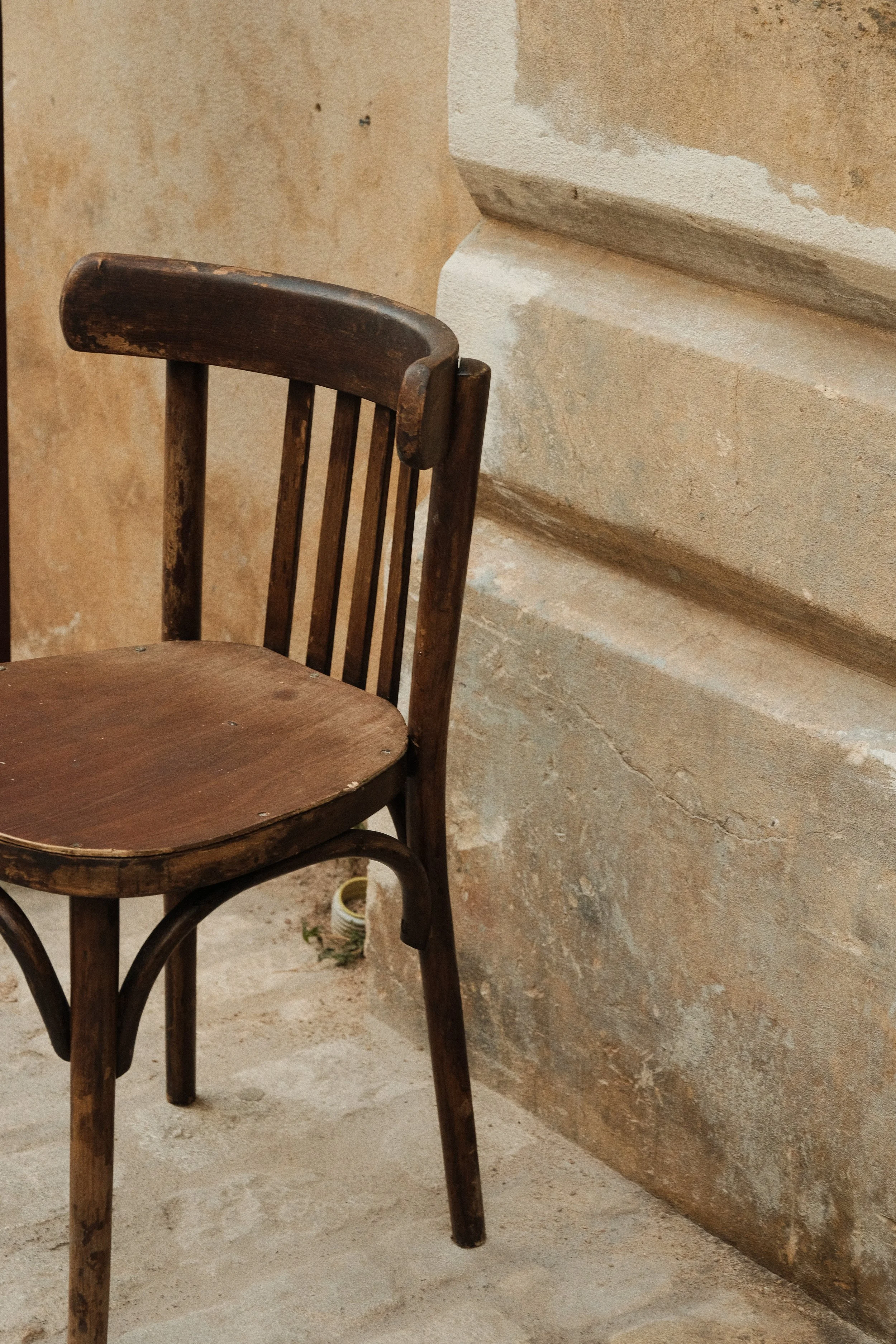Alte, abgenutzte Holzstuhl vor einer beigen Wand mit Putzrissen