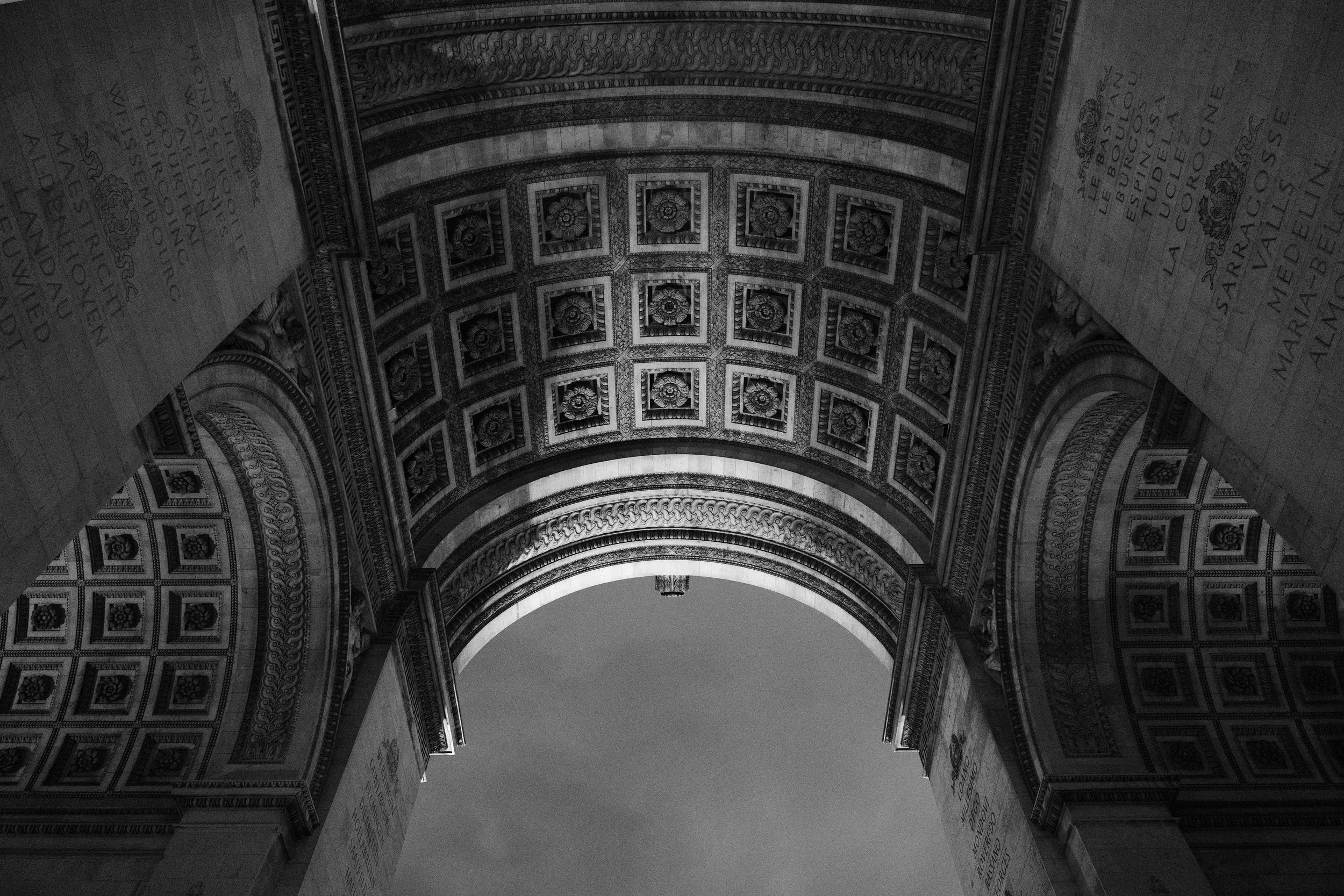 Blick nach oben auf die Innenseite eines prächtigen Triumphbogens mit kunstvoll verzierten Details in Schwarz-Weiß