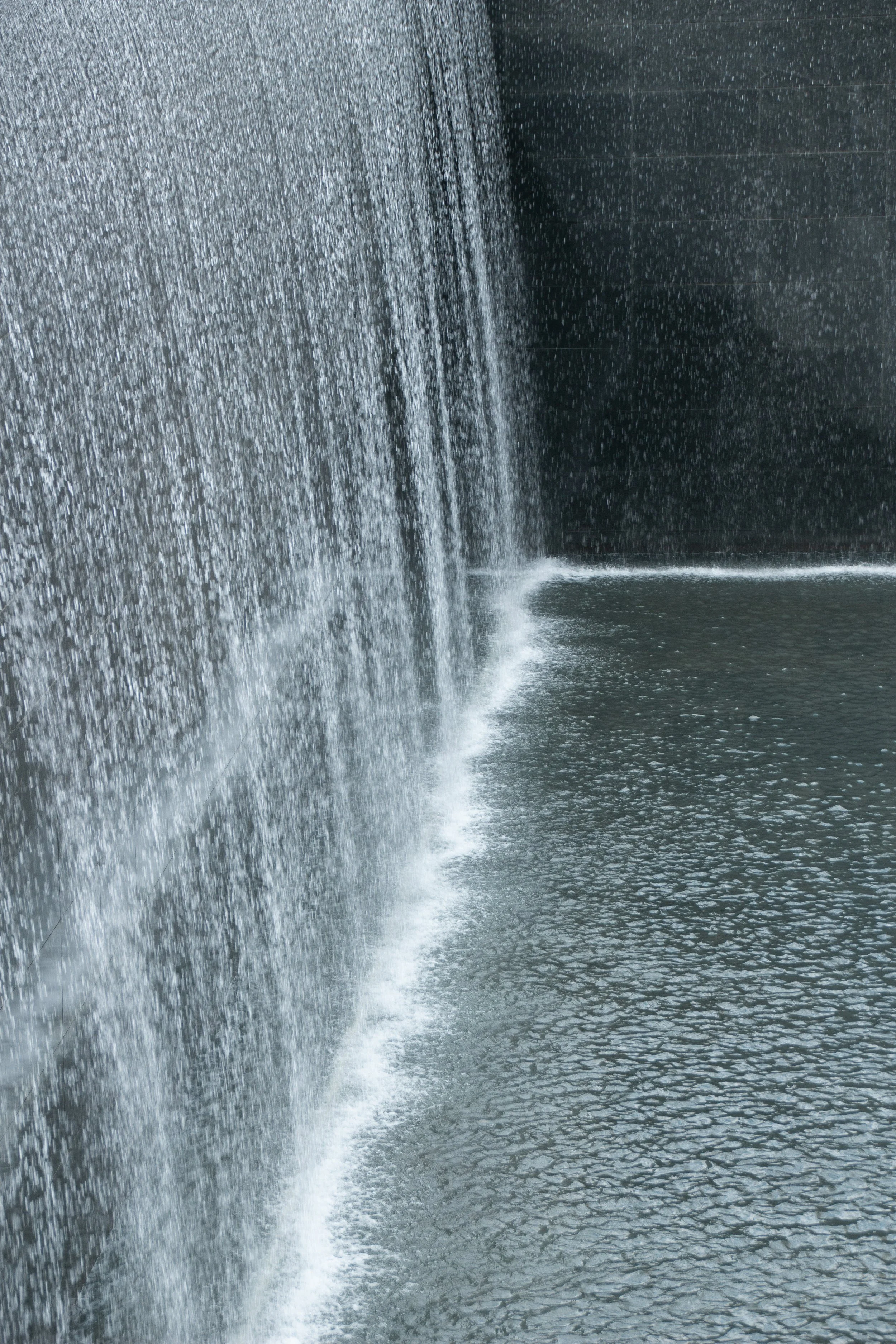Nahaufnahme eines Wasserfalls, der Wasser über eine schwarze Steinwand ins Becken darunter stürzt.