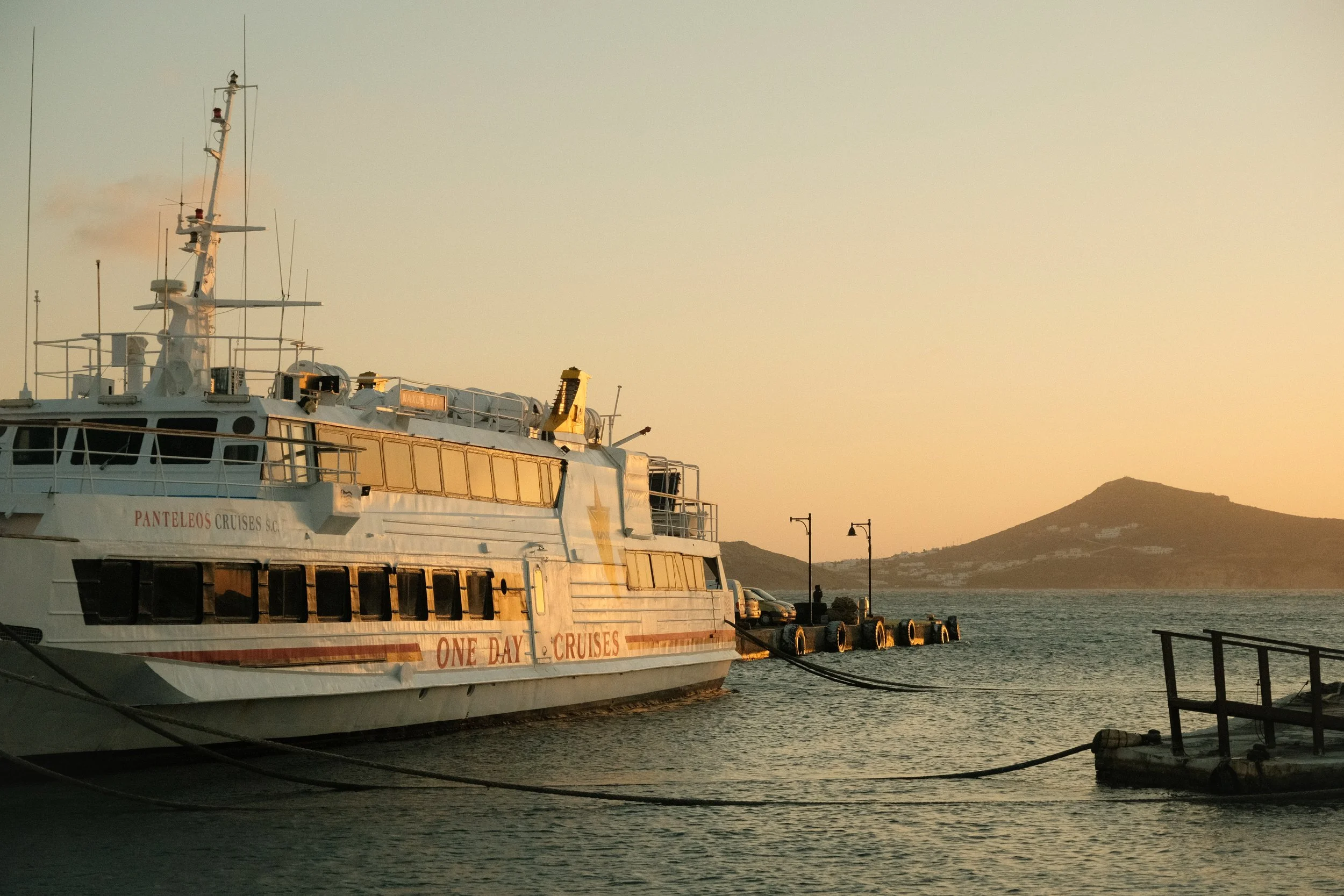 Segelschiff namens 'One Day Cruises' im Hafen bei Sonnenuntergang, mit Blick auf einen Hügel im Hintergrund.