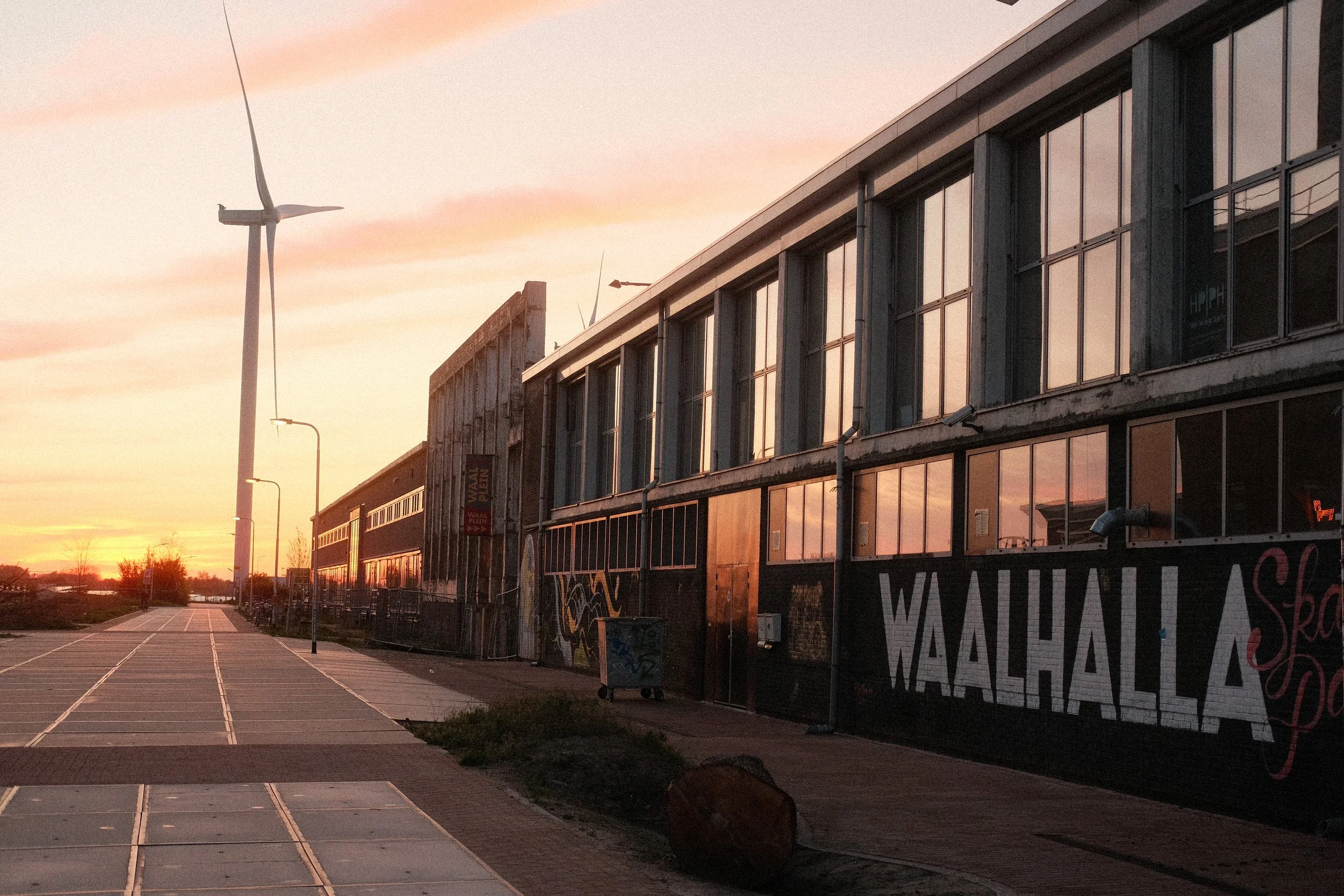Ein urbaner Straßenzug bei Sonnenuntergang mit alten Gebäuden und einem Windrad im Hintergrund.