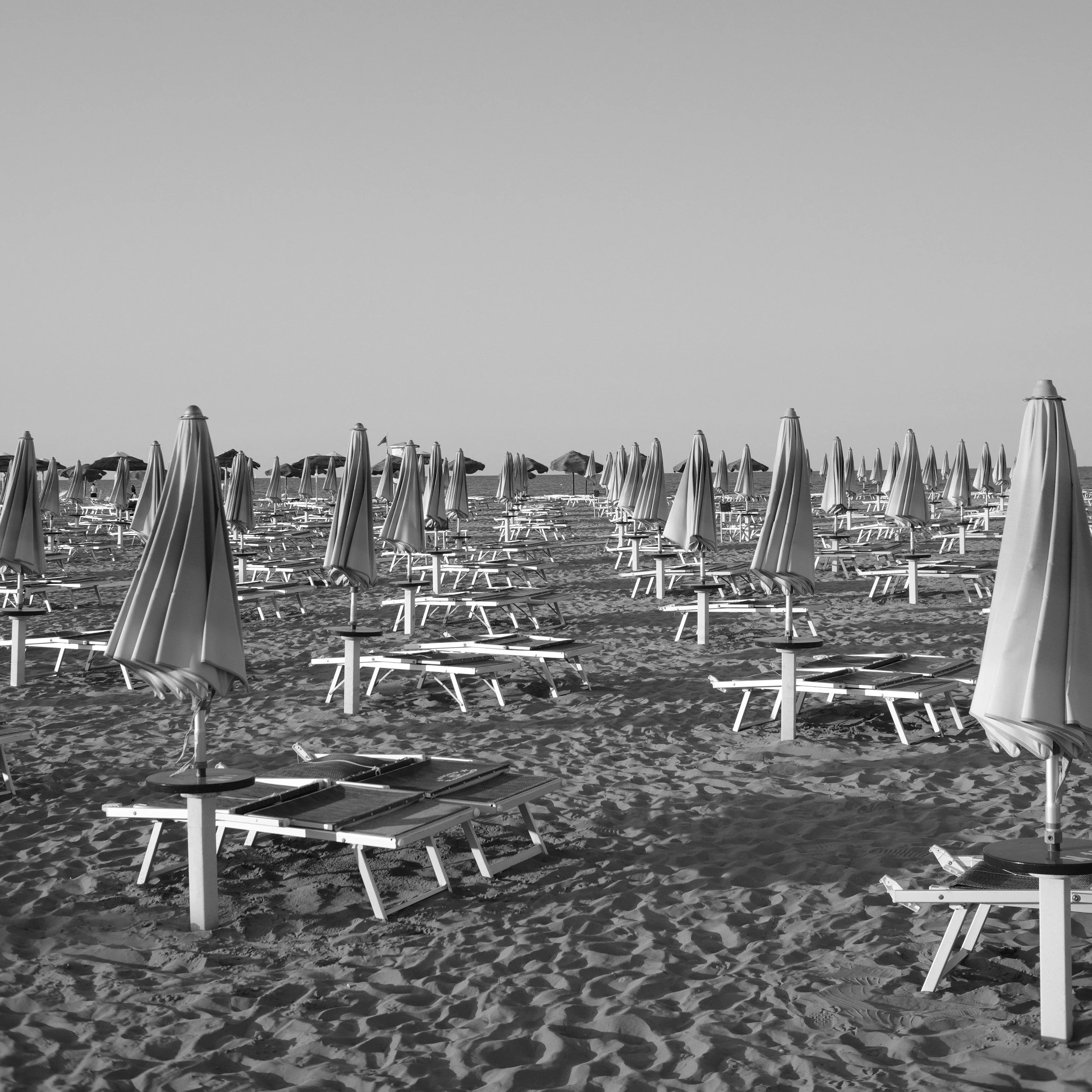 Leerer Strand mit geschlossenem Sonnenschirm und Liegestühlen in schwarz-weiß