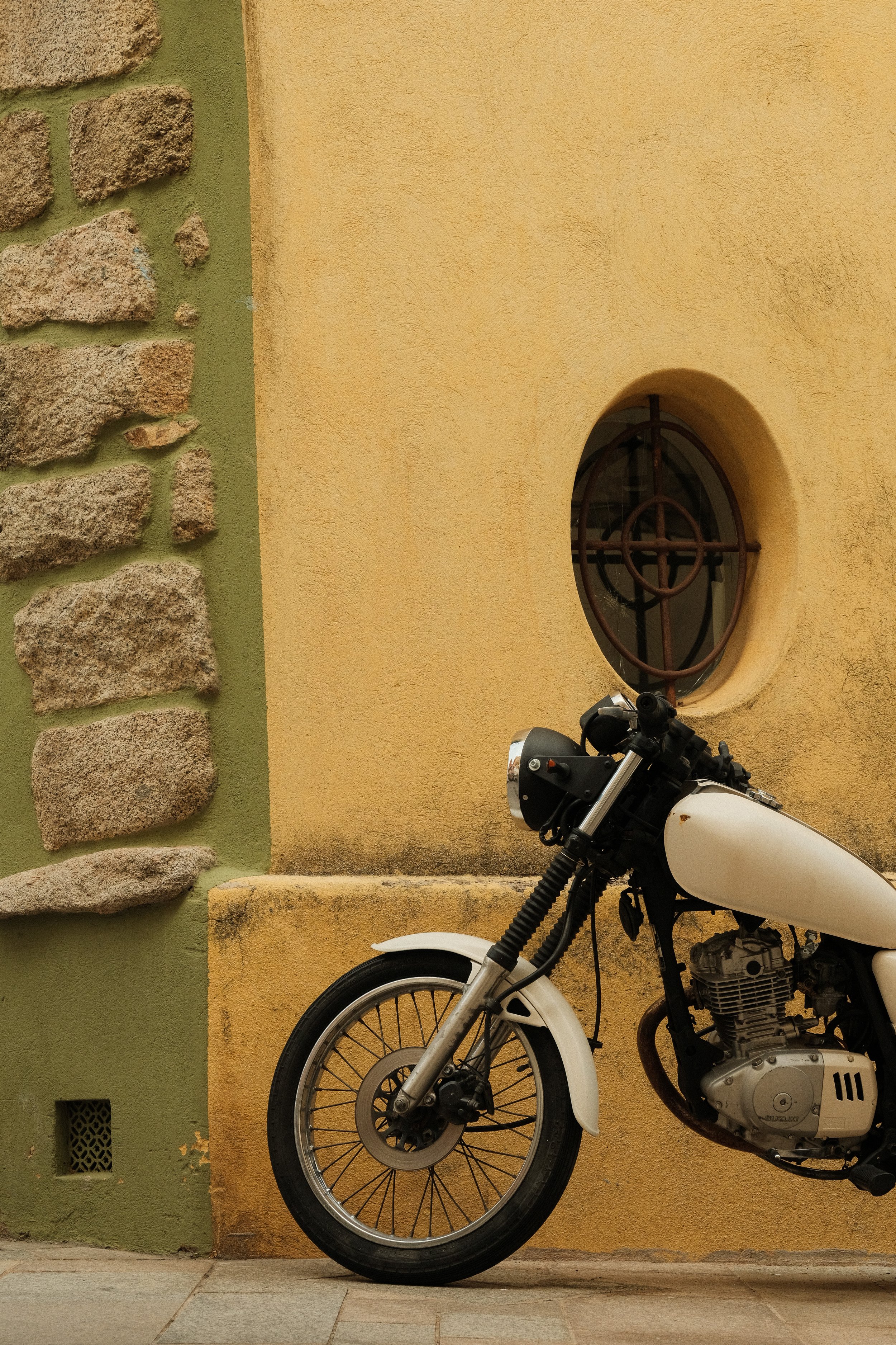 Ein weißes Motorrad parkt vor einer gelben Wand mit einem kleinen runden Fenster mit Metallgitter