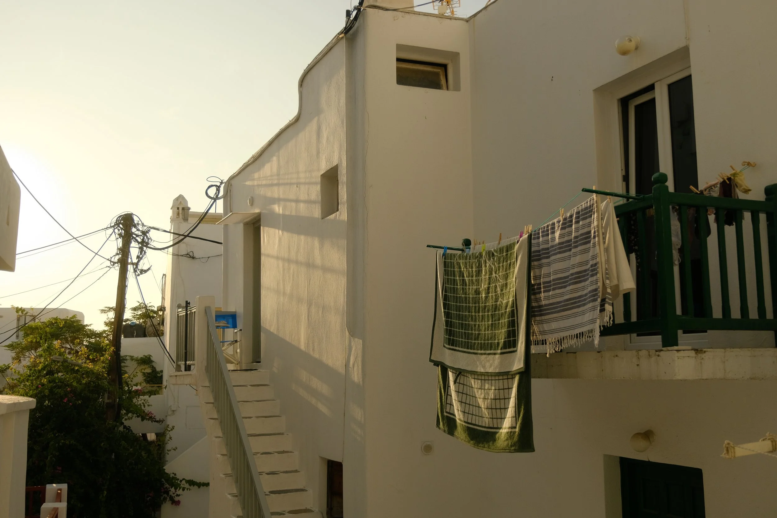 Weiße Gebäudefassade mit Balkon, Wäschestangen und Wäsche, Sonnenlicht, Stromleitungen.