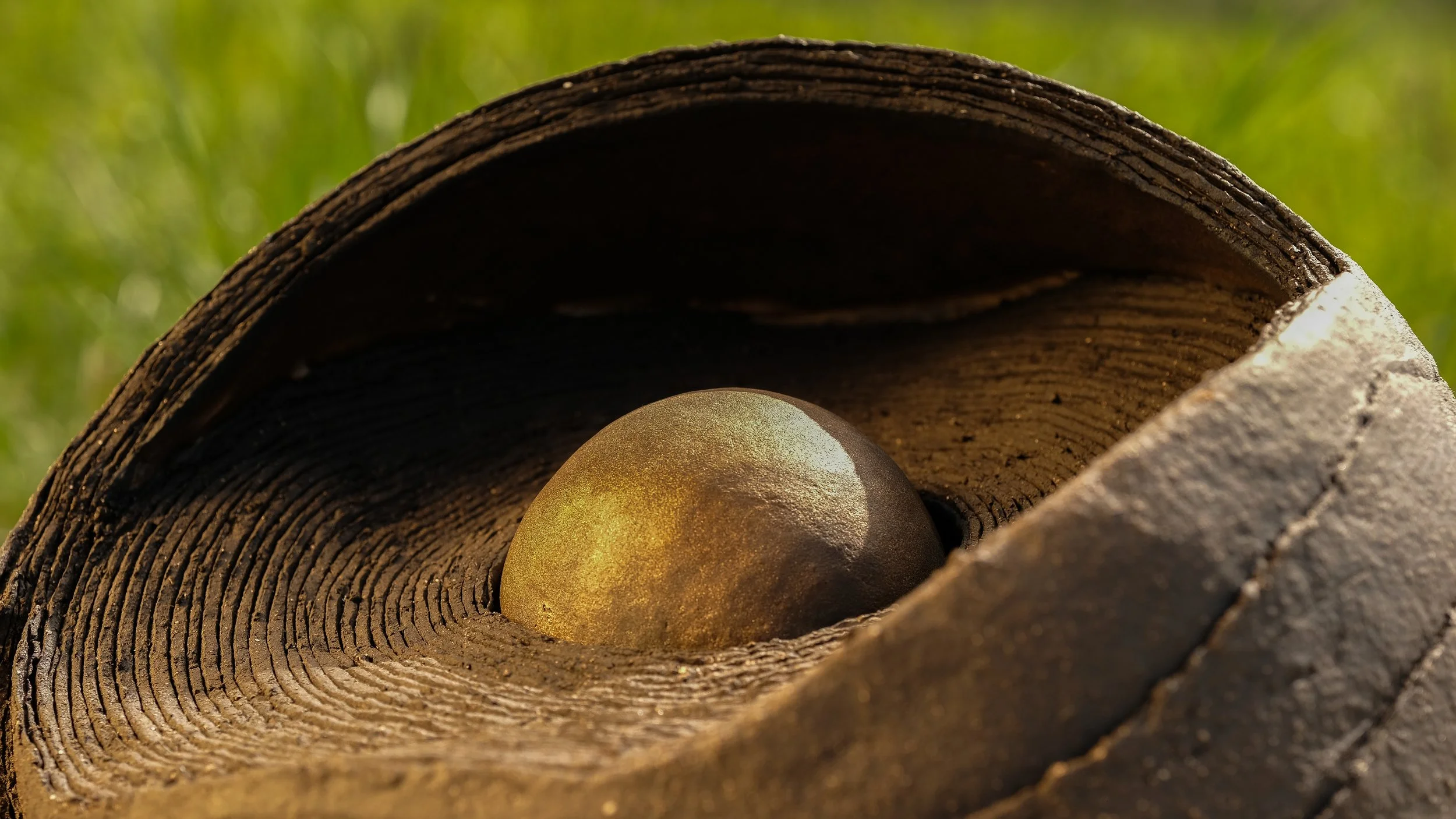 Eine alte, braune Basketball mit einer glatten Oberfläche, liegt im Inneren eines Kegels aus Holz, der von einer grünen, unscharfen Wiese im Hintergrund umgeben ist.