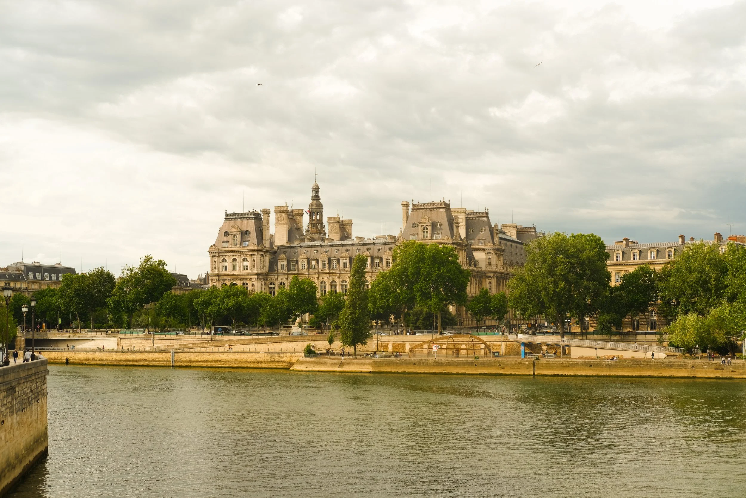 Historisches Gebäude am Ufer eines Flusses, umgeben von Bäumen, bei bewölktem Himmel, in Paris.