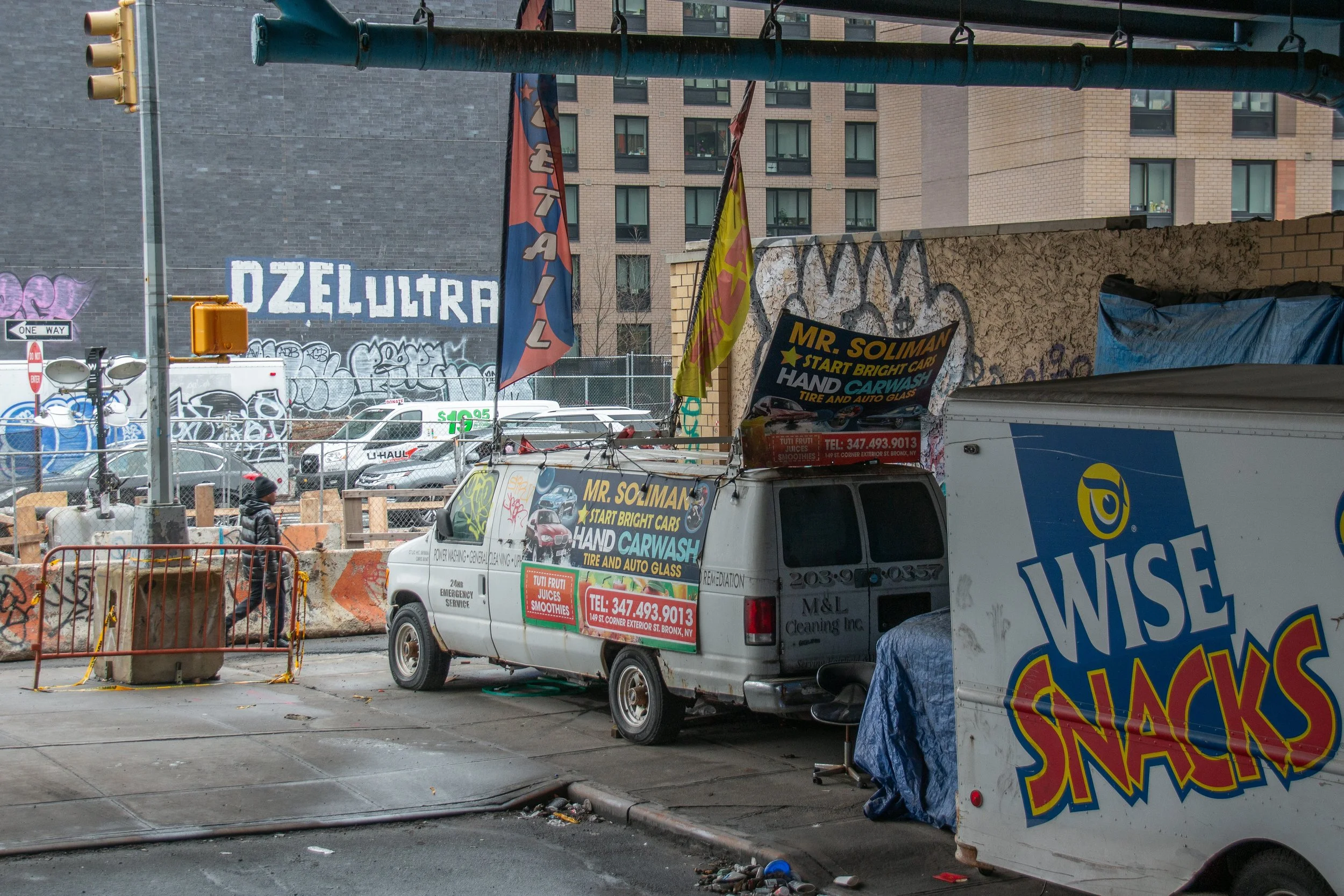 Straßenszene mit Verkaufswagen und einem Food-Truck, umgeben von Graffiti und Bauzäunen in einer urbanen Umgebung.