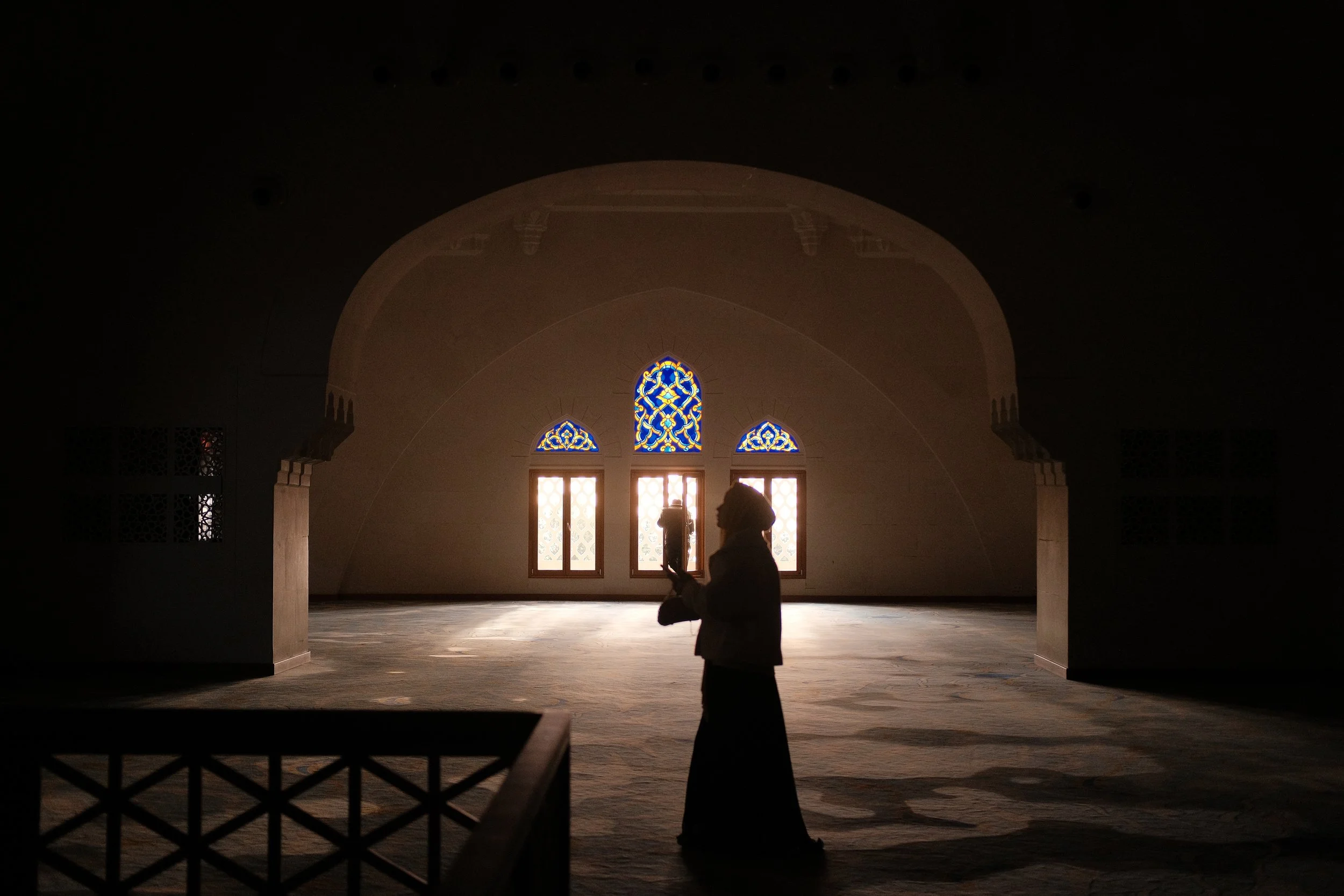 Silhouette einer Person in einem großen, leeren Raum mit hohen, dekorativen Fenstern und buntem Glas.
