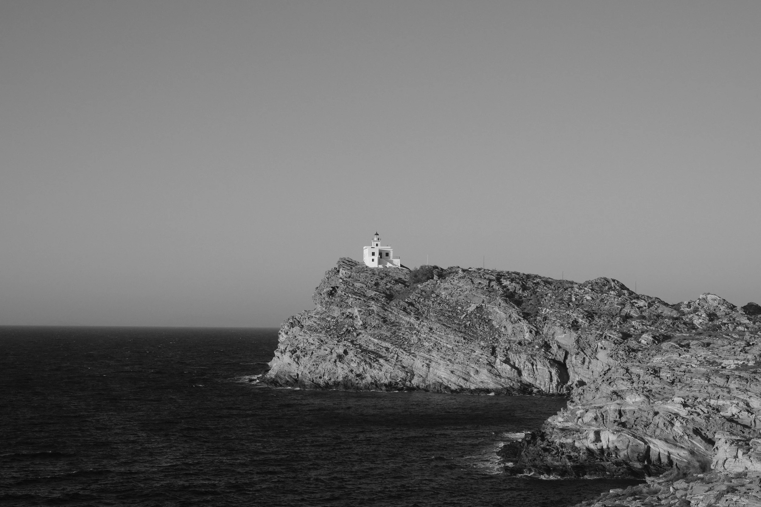 Leuchtturm auf felsiger Küste im Meer, schwarz-weiß Aufnahme.