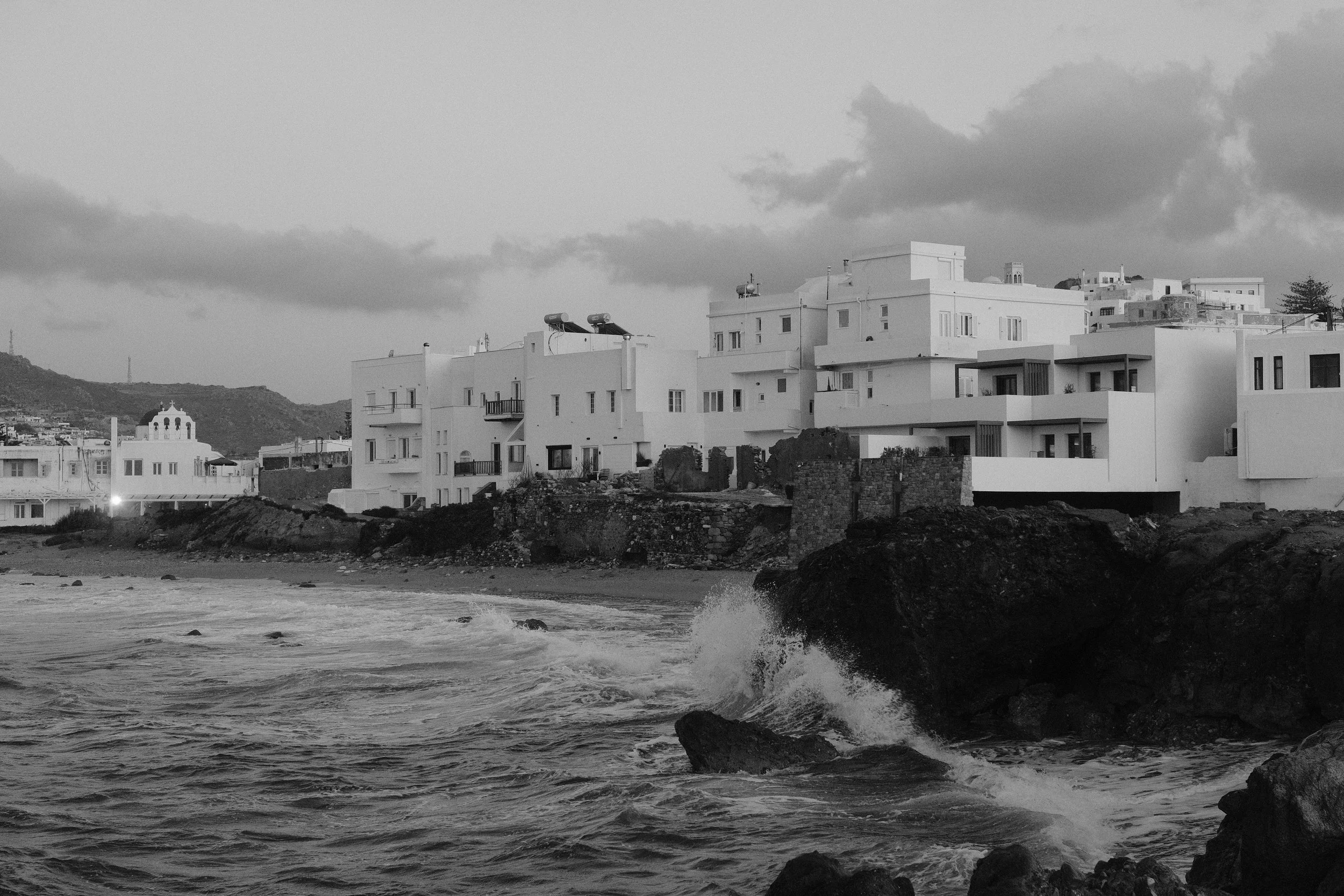 Küstenlandschaft mit weißen, modernen Gebäuden und Wasser, das gegen Felsen schlägt.